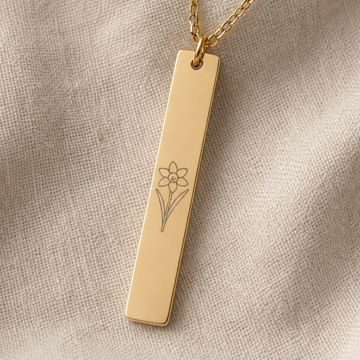 December birth flower necklace — Narcissus engraved vertical bar pendant flatlay with dried botanicals on cream linen