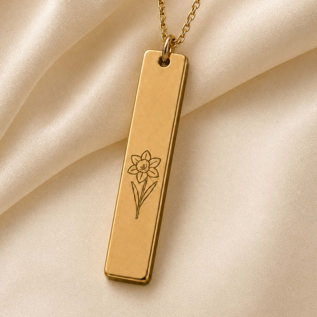 March birth flower necklace — Daffodil engraved vertical bar pendant flatlay with dried botanicals on cream linen, premium editorial styling, 18K Gold PVD on premium 316L stainless steel