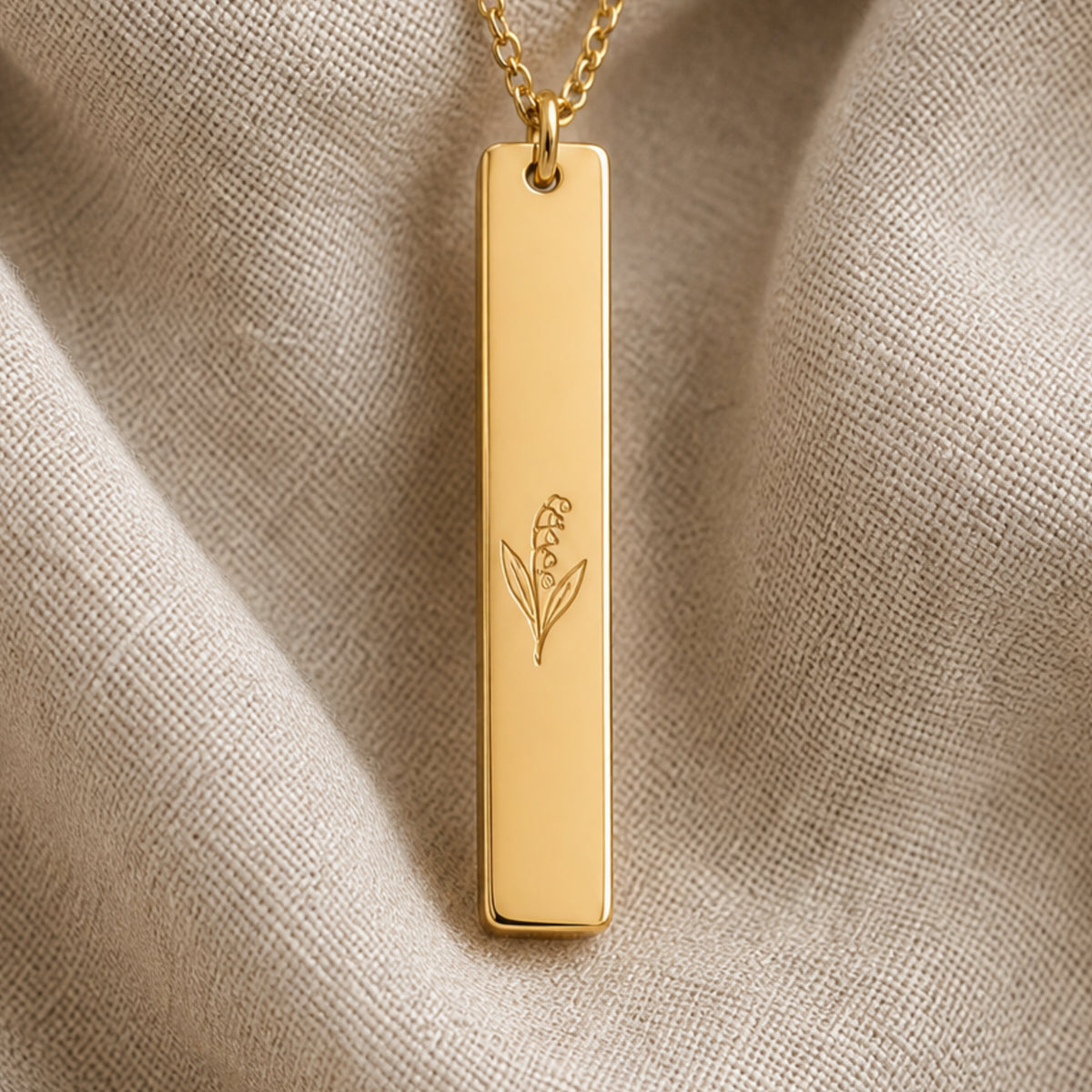 May birth flower necklace — Lily of the Valley engraved vertical bar pendant flatlay with dried botanicals on cream linen