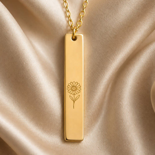 April birth flower necklace — Daisy engraved vertical bar pendant flatlay with dried botanicals on cream linen