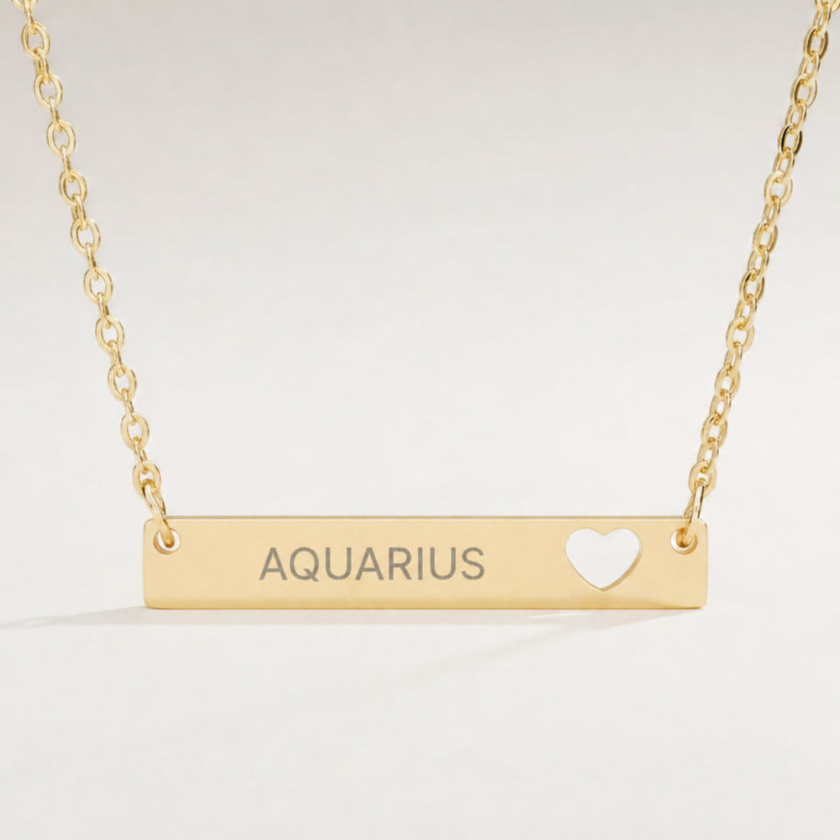 Aquarius zodiac necklace close-up — 18K Gold polished cutout heart bar pendant with grey laser-etched AQUARIUS, see-through heart cutout, premium macro on clean background