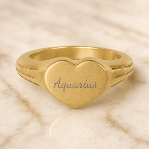 Aquarius zodiac heart signet ring — hero macro of laser-engraved Aquarius name in Dancing Script cursive on 18K gold heart face