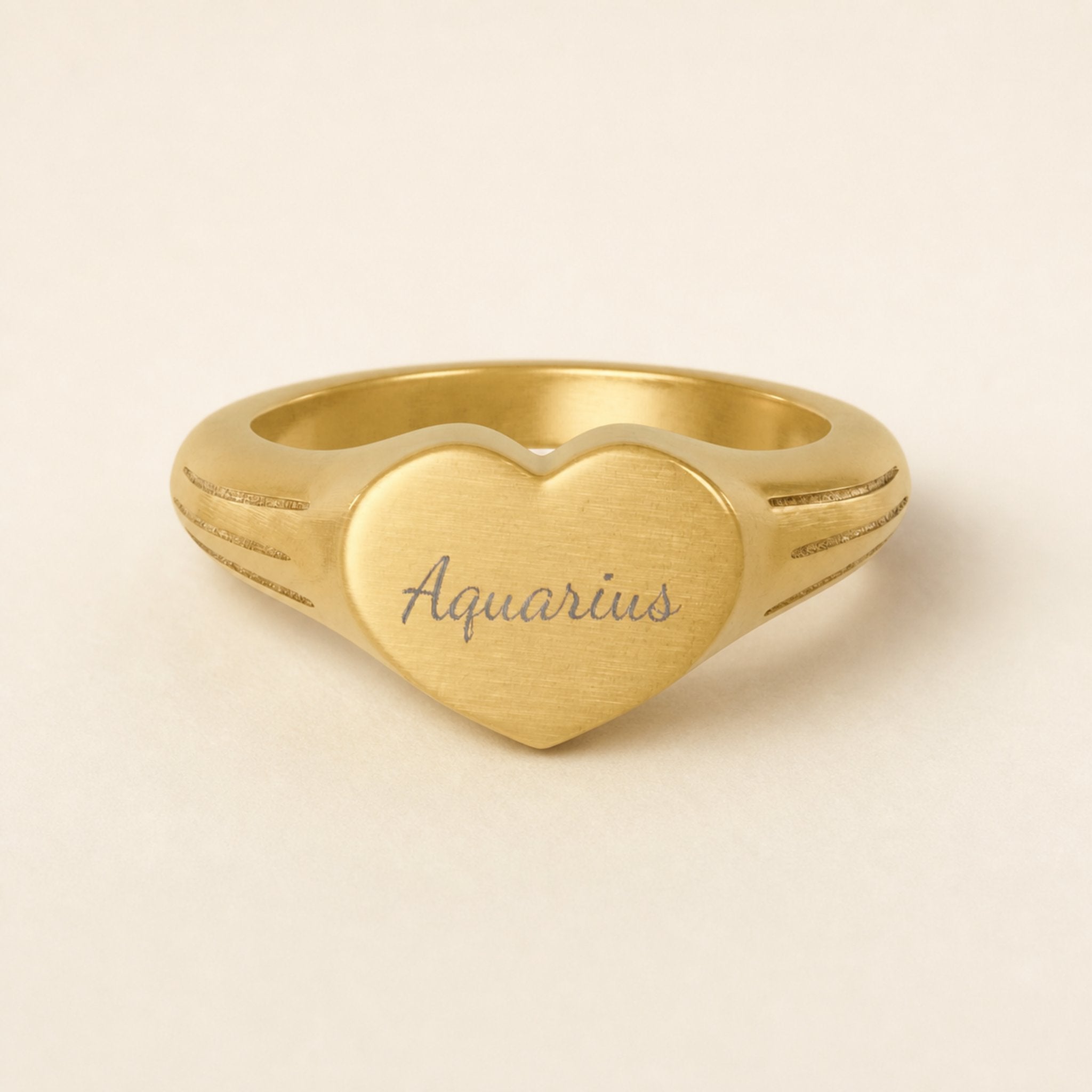 Aquarius zodiac heart signet ring studio front — clean cream backdrop product shot, 18K gold matte PVD