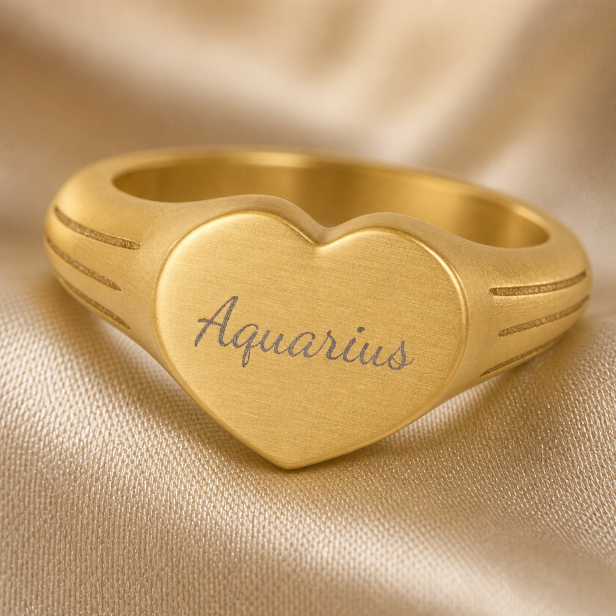 Aquarius zodiac heart signet ring engraving close-up — laser-etched Aquarius name detail, brushed grey cursive on matte gold heart
