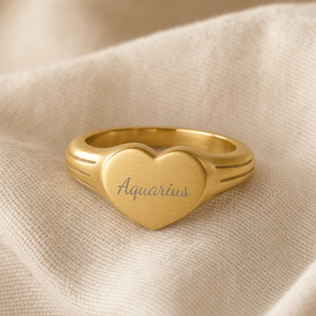 Aquarius zodiac heart signet ring linen flatlay — engraved Aquarius heart ring on rumpled cream linen with dried floral, editorial styling