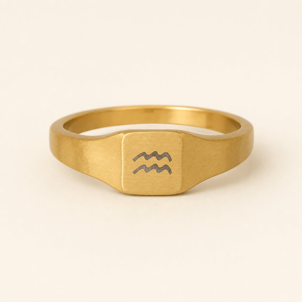 Aquarius zodiac square signet ring studio front — clean cream backdrop product shot, 18K gold matte PVD
