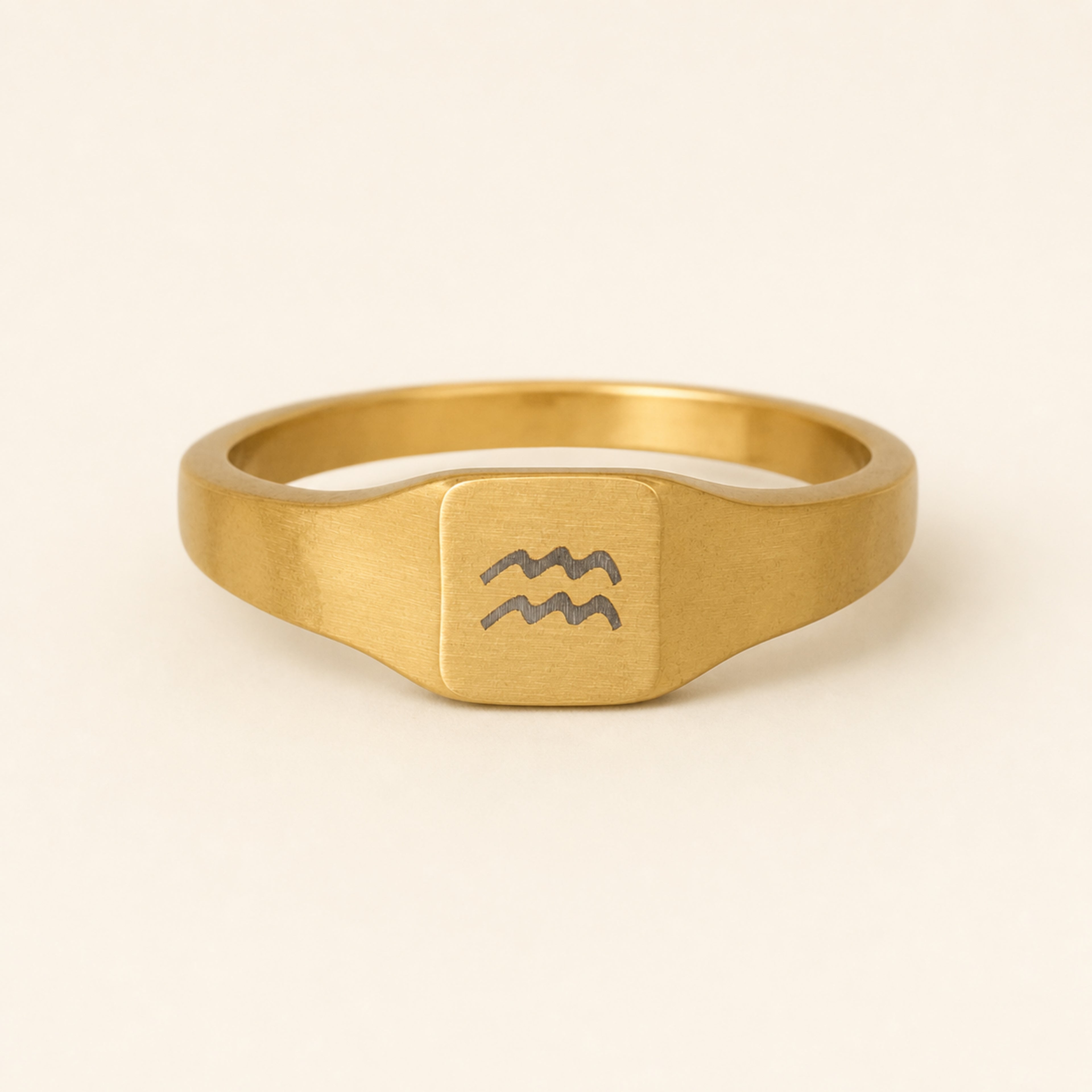 Aquarius zodiac square signet ring studio front — clean cream backdrop product shot, 18K gold matte PVD