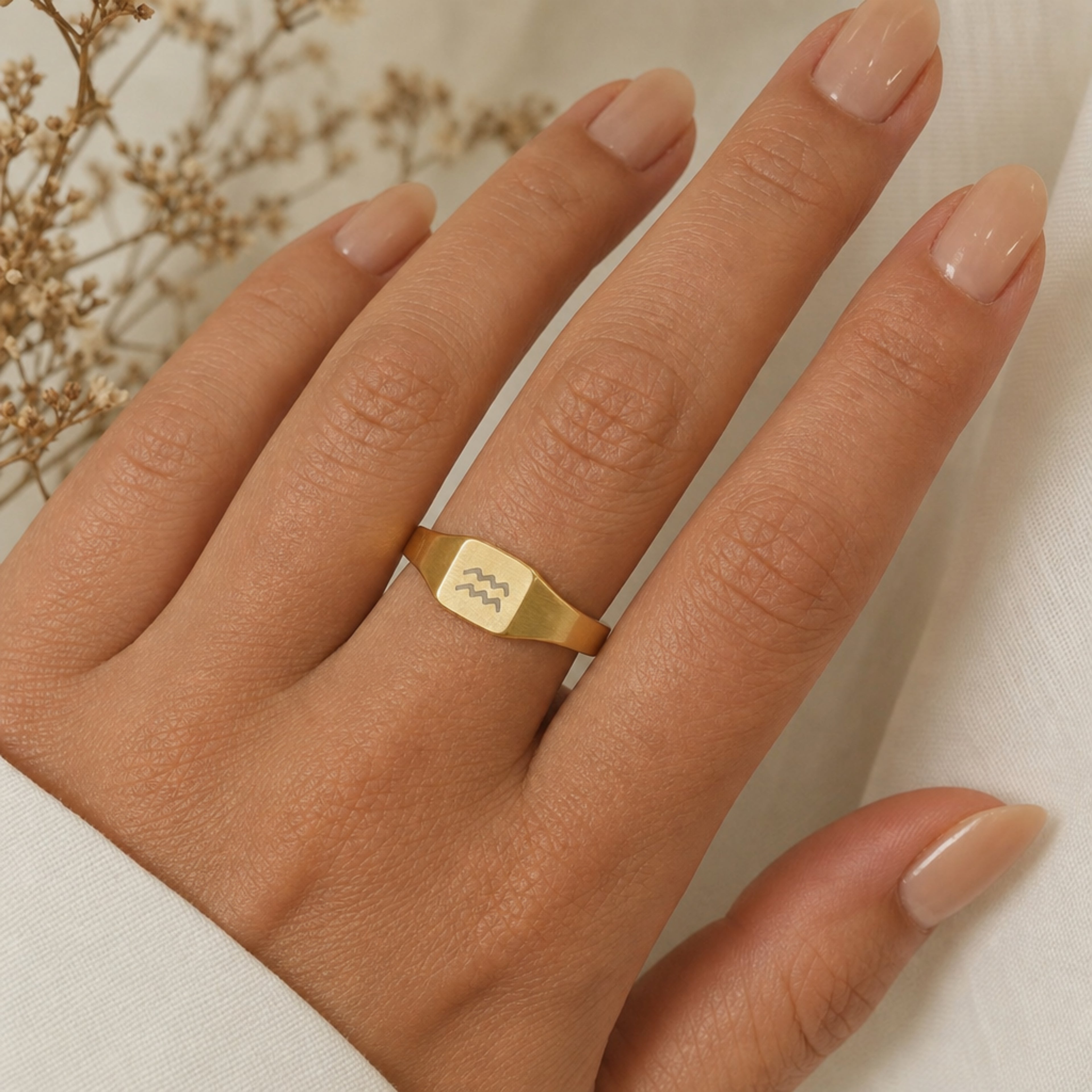 Aquarius zodiac square signet ring on finger — model wearing engraved Aquarius signet, cream linen lifestyle moment