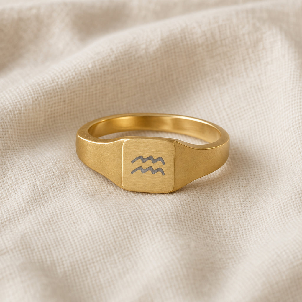 Aquarius zodiac square signet ring linen flatlay — engraved Water-bearer waves ring on rumpled cream linen, editorial product shot
