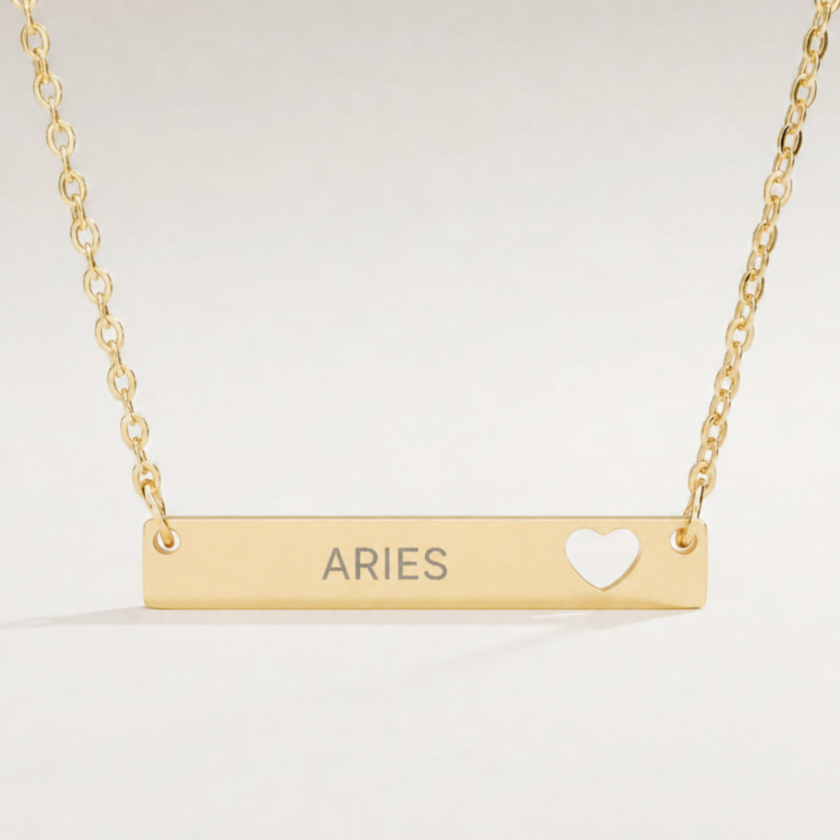 Aries zodiac necklace — engraved horizontal cutout heart bar pendant, premium close-up macro hero, 18K Gold PVD polished mirror, grey laser-etched ARIES, see-through heart cutout, 316L stainless steel