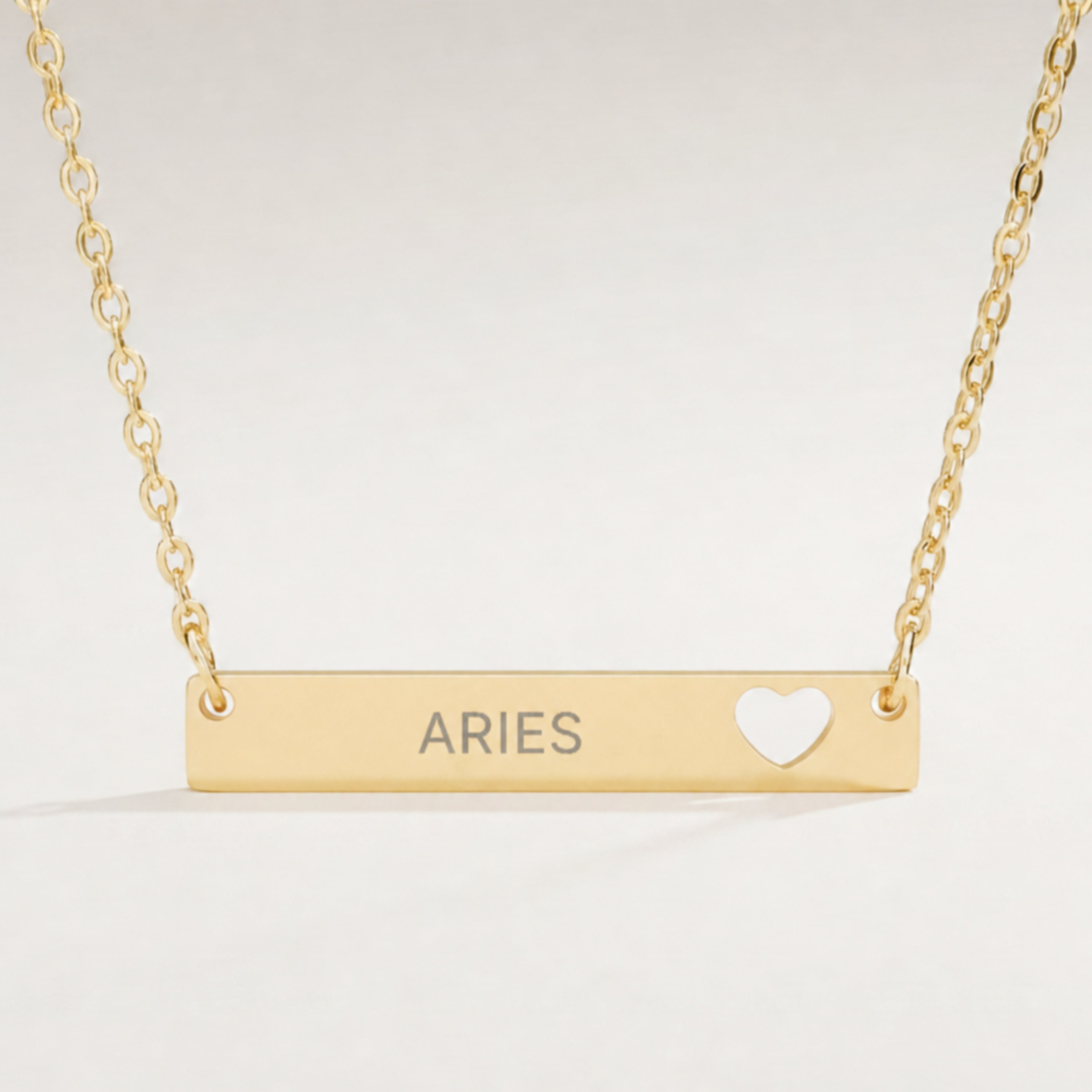 Aries zodiac necklace — engraved horizontal cutout heart bar pendant, premium close-up macro hero, 18K Gold PVD polished mirror, grey laser-etched ARIES, see-through heart cutout, 316L stainless steel