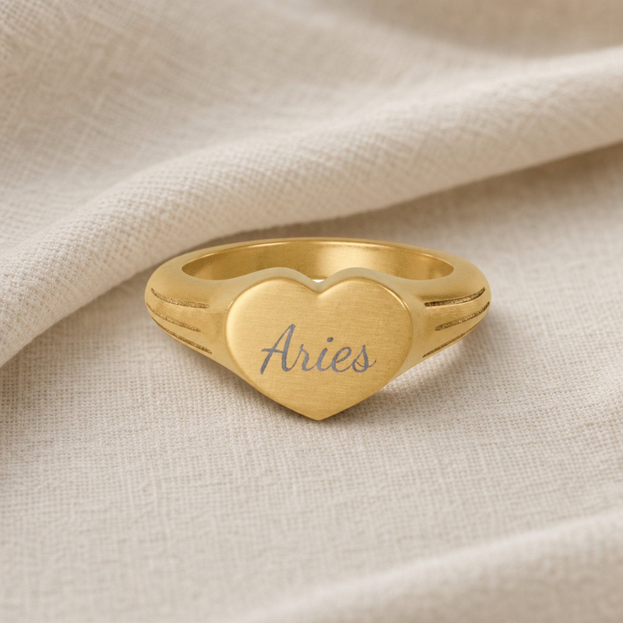 Aries zodiac heart signet ring linen flatlay — engraved Aries heart ring on rumpled cream linen with dried floral, editorial styling