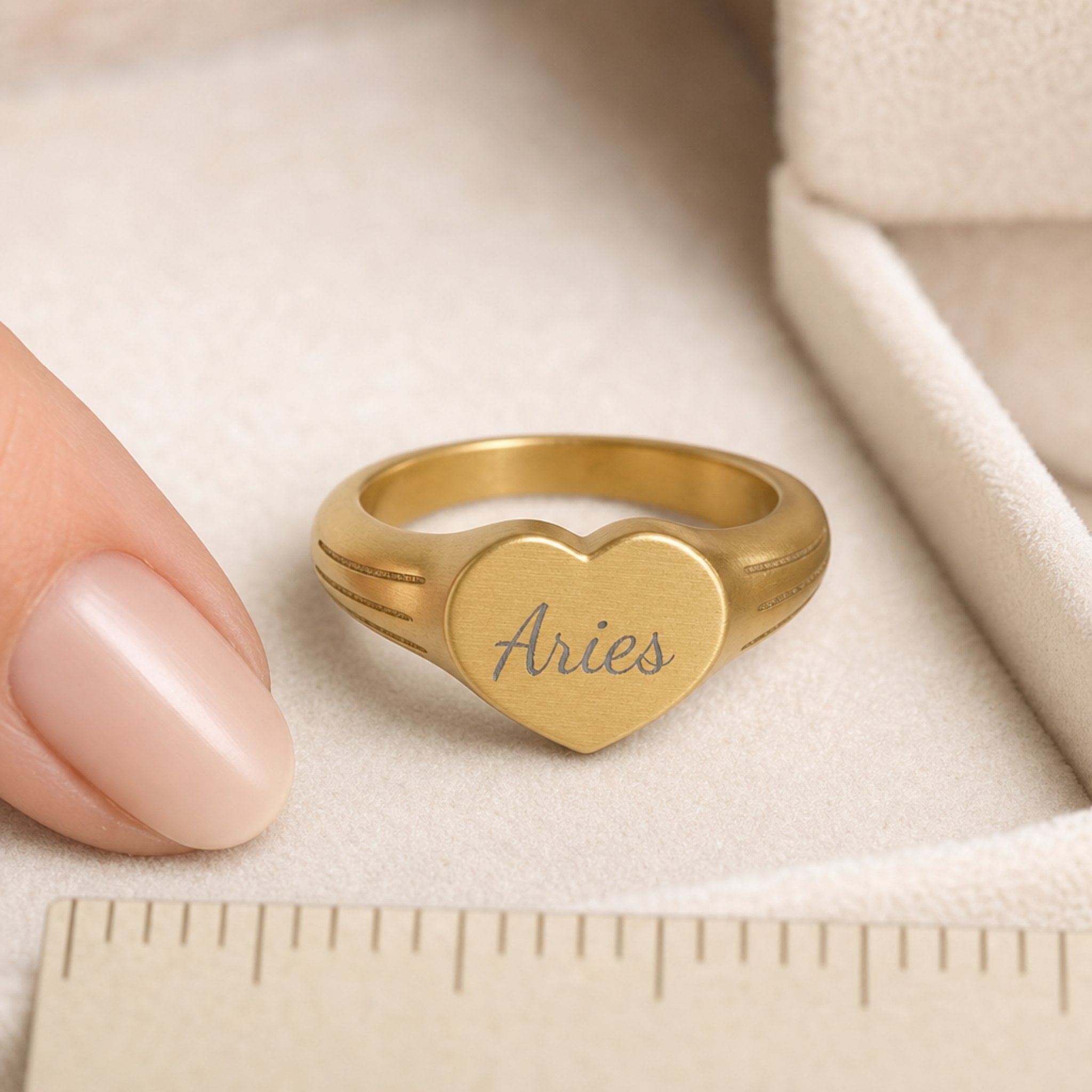 Aries zodiac heart signet ring scale-in-hand — fingers holding heart ring next to gift box and ruler, dainty signet sizing