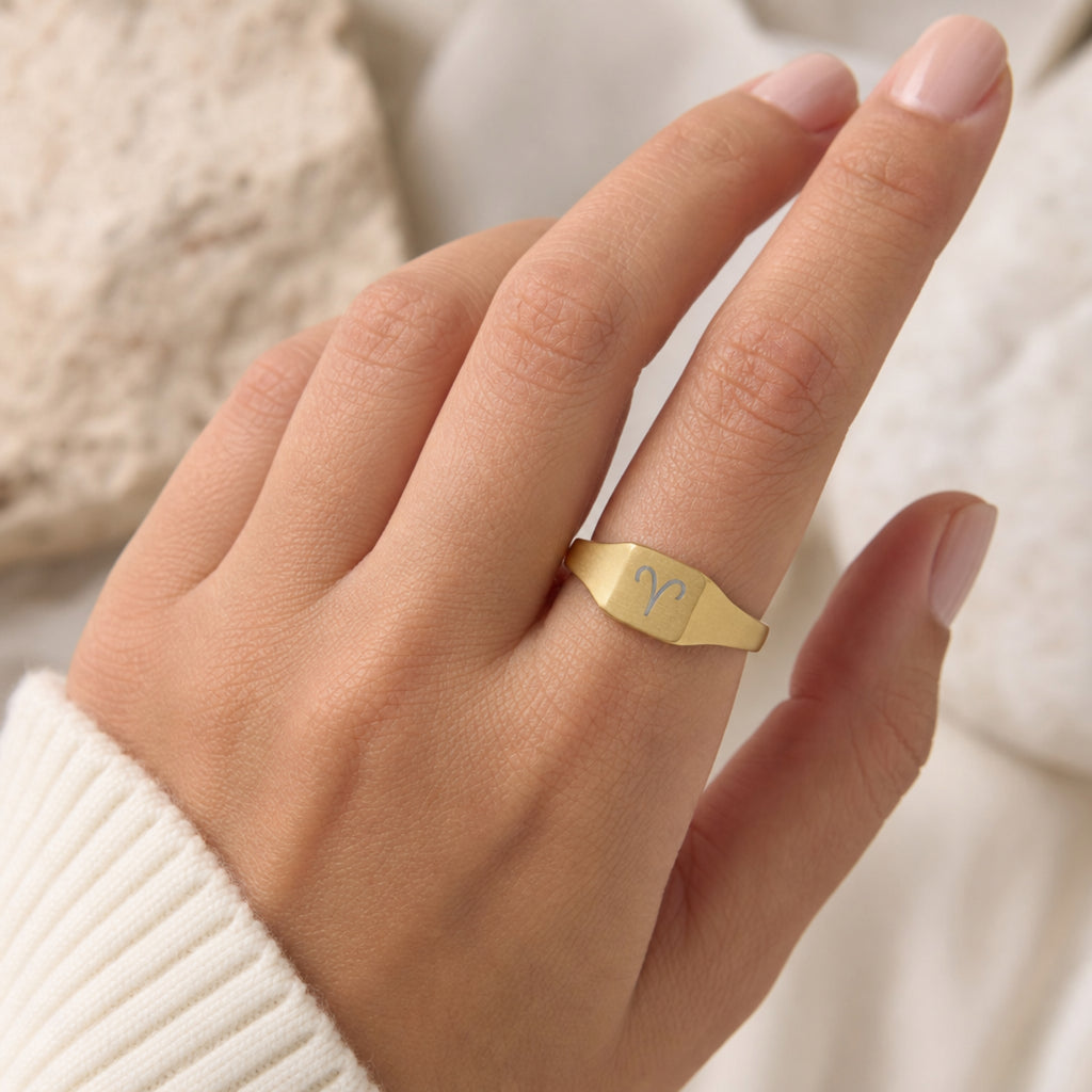 Aries zodiac square signet ring on finger — model wearing engraved Aries signet, cream linen lifestyle moment