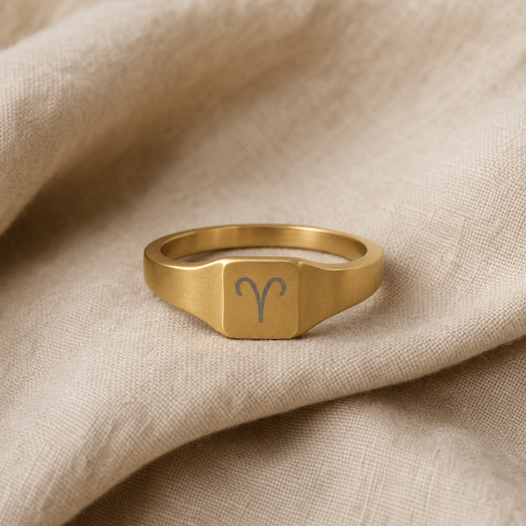 Aries zodiac square signet ring linen flatlay — engraved Ram ring on rumpled cream linen, editorial product shot