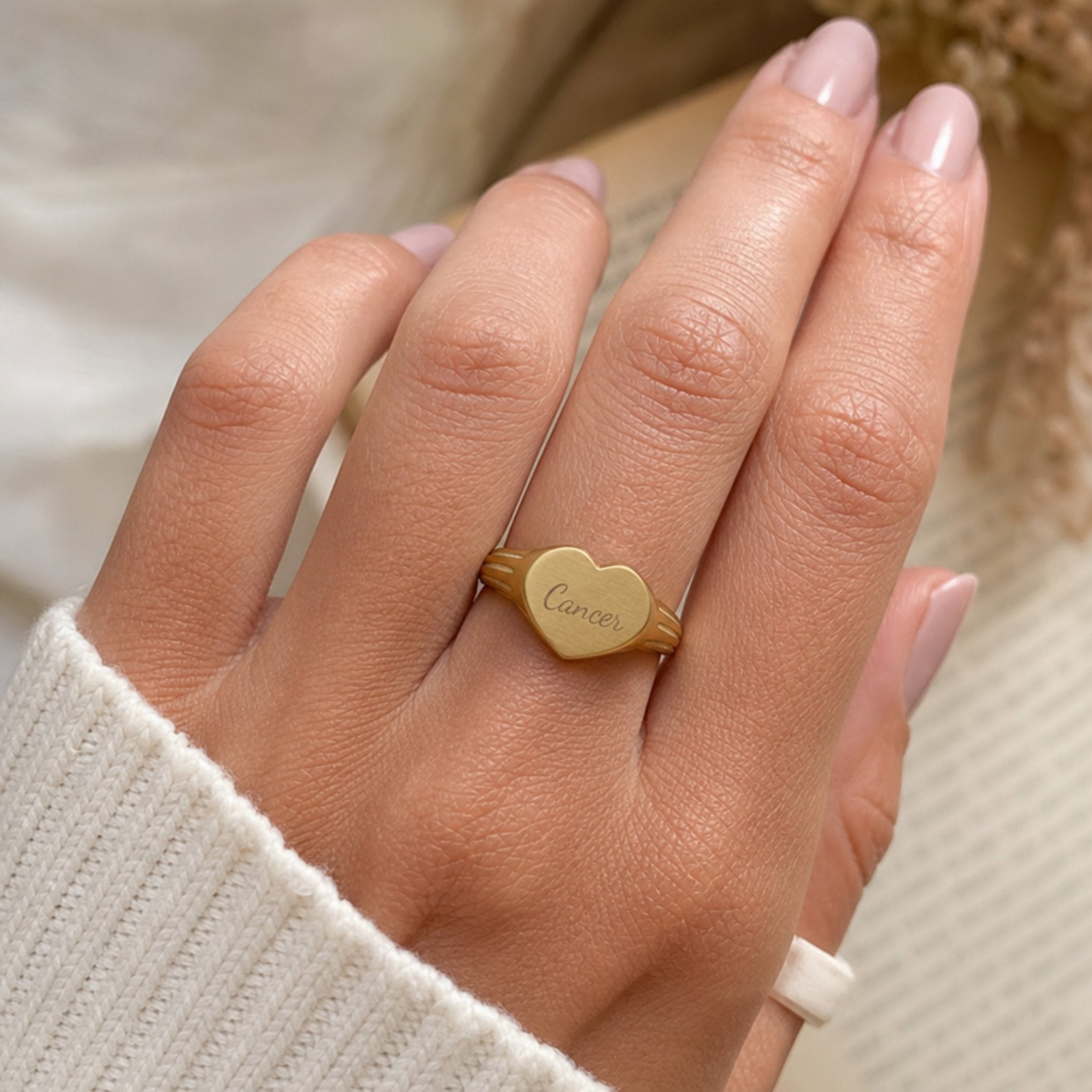 Cancer zodiac heart signet ring on finger — model wearing engraved Cancer heart signet, cream linen lifestyle moment