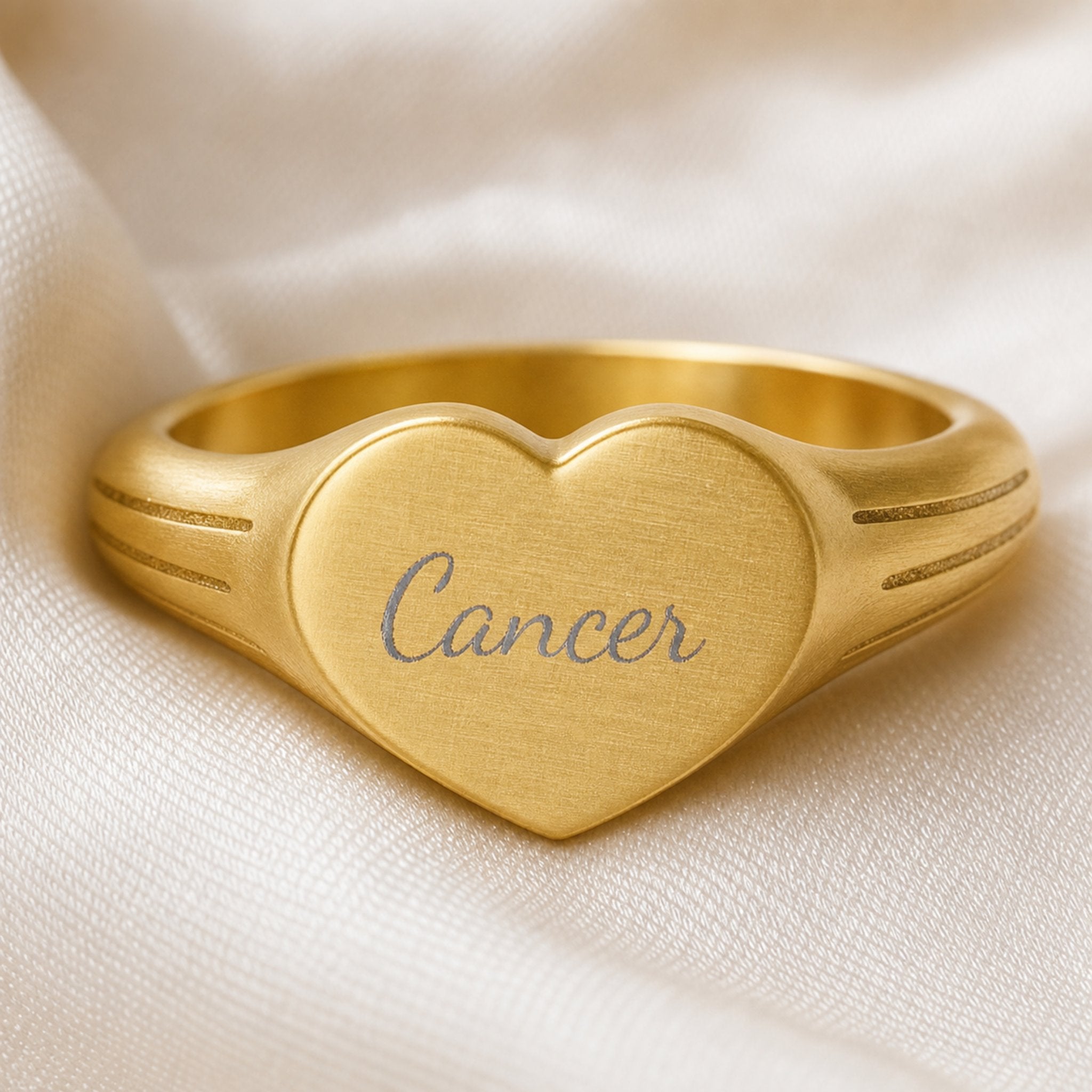 Cancer zodiac heart signet ring engraving close-up — laser-etched Cancer name detail, brushed grey cursive on matte gold heart