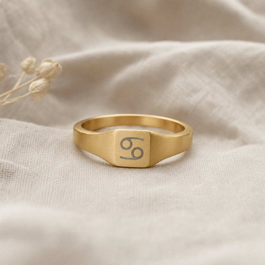 Cancer zodiac square signet ring linen flatlay — engraved Crab ring on rumpled cream linen, editorial product shot