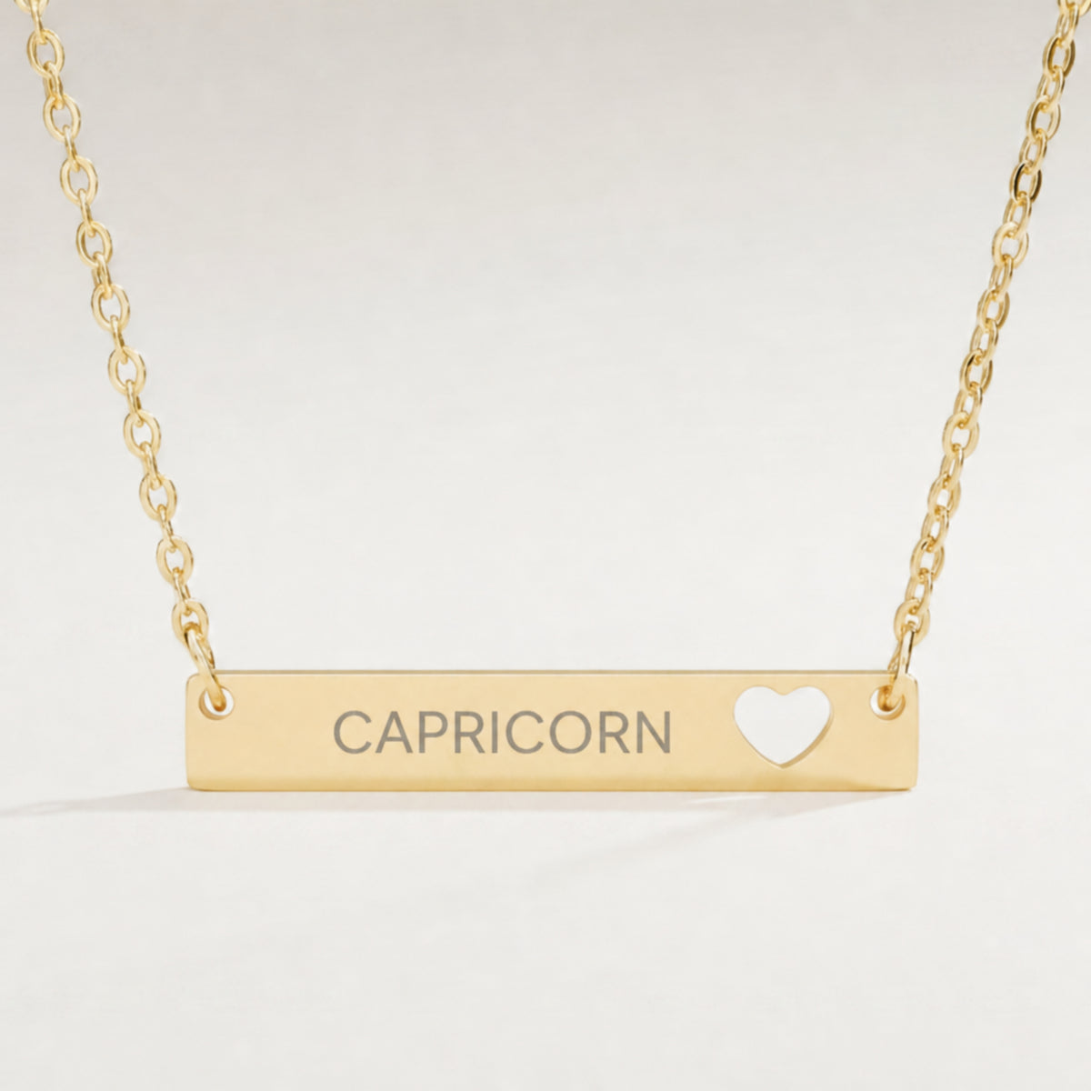 Capricorn zodiac necklace close-up — 18K Gold polished cutout heart bar pendant with grey laser-etched CAPRICORN, see-through heart cutout, premium macro on clean background