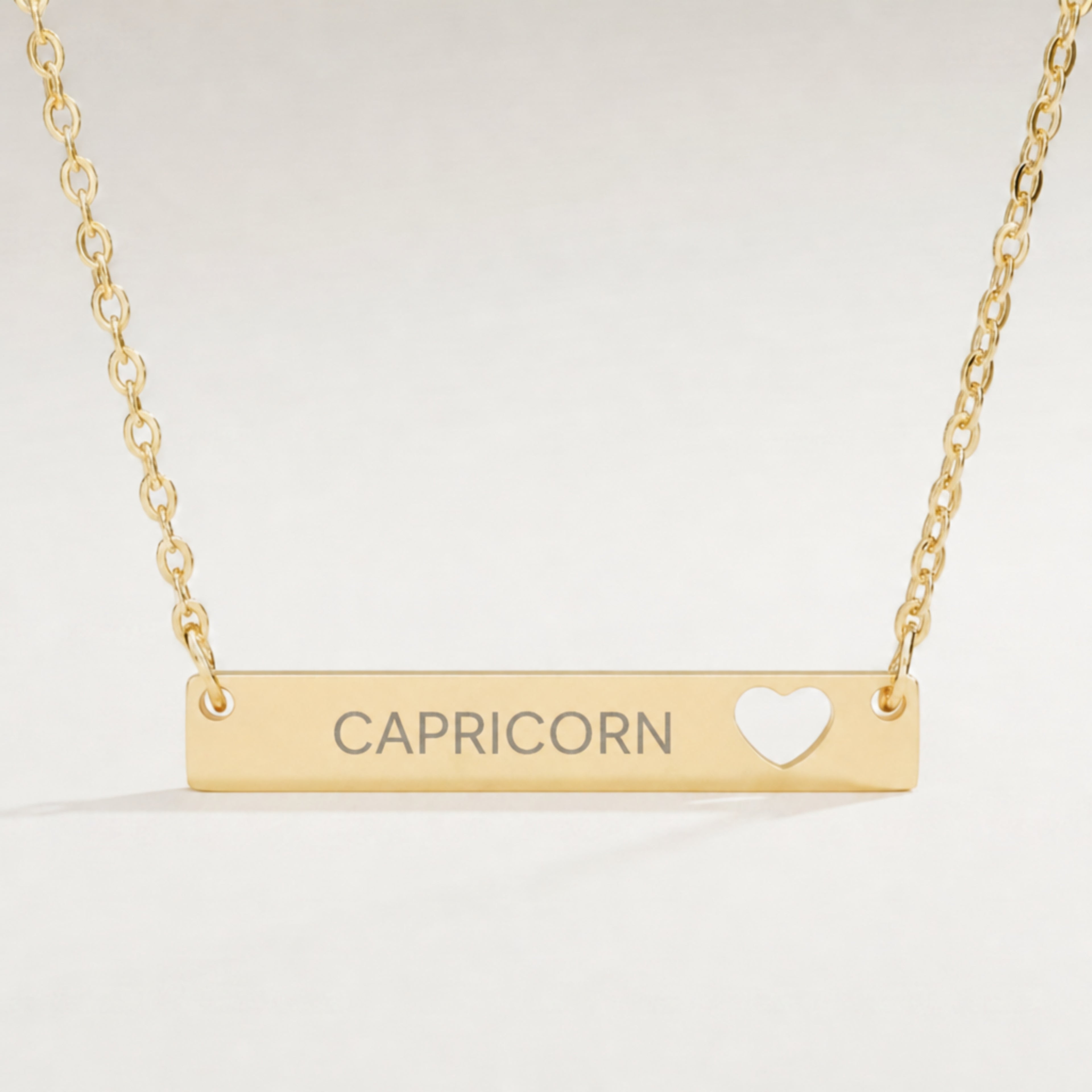 Capricorn zodiac necklace close-up — 18K Gold polished cutout heart bar pendant with grey laser-etched CAPRICORN, see-through heart cutout, premium macro on clean background