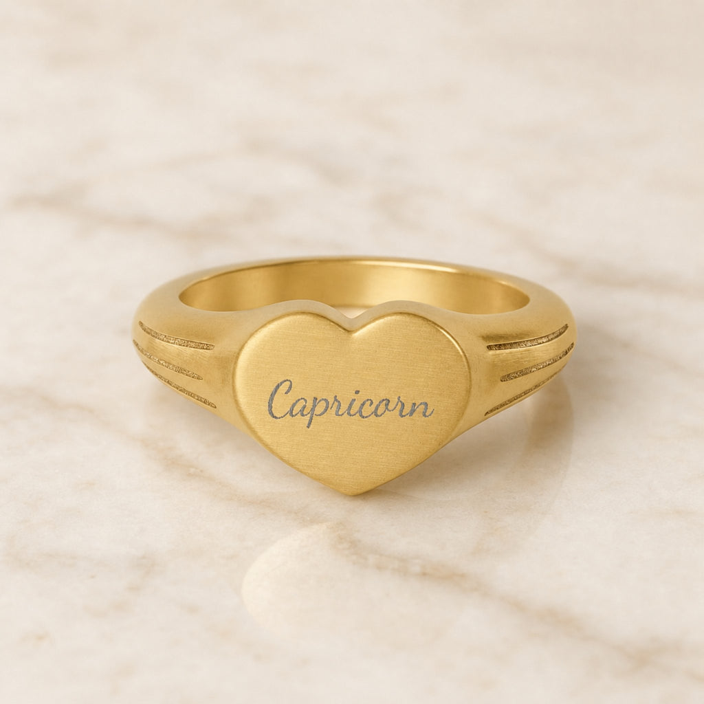 Capricorn zodiac heart signet ring — hero macro of laser-engraved Capricorn name in Dancing Script cursive on 18K gold heart face