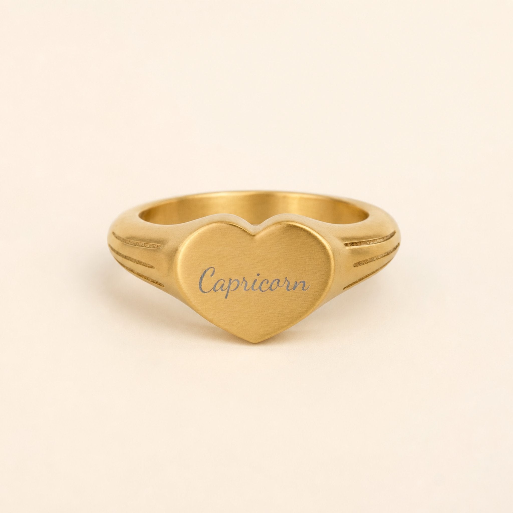Capricorn zodiac heart signet ring studio front — clean cream backdrop product shot, 18K gold matte PVD