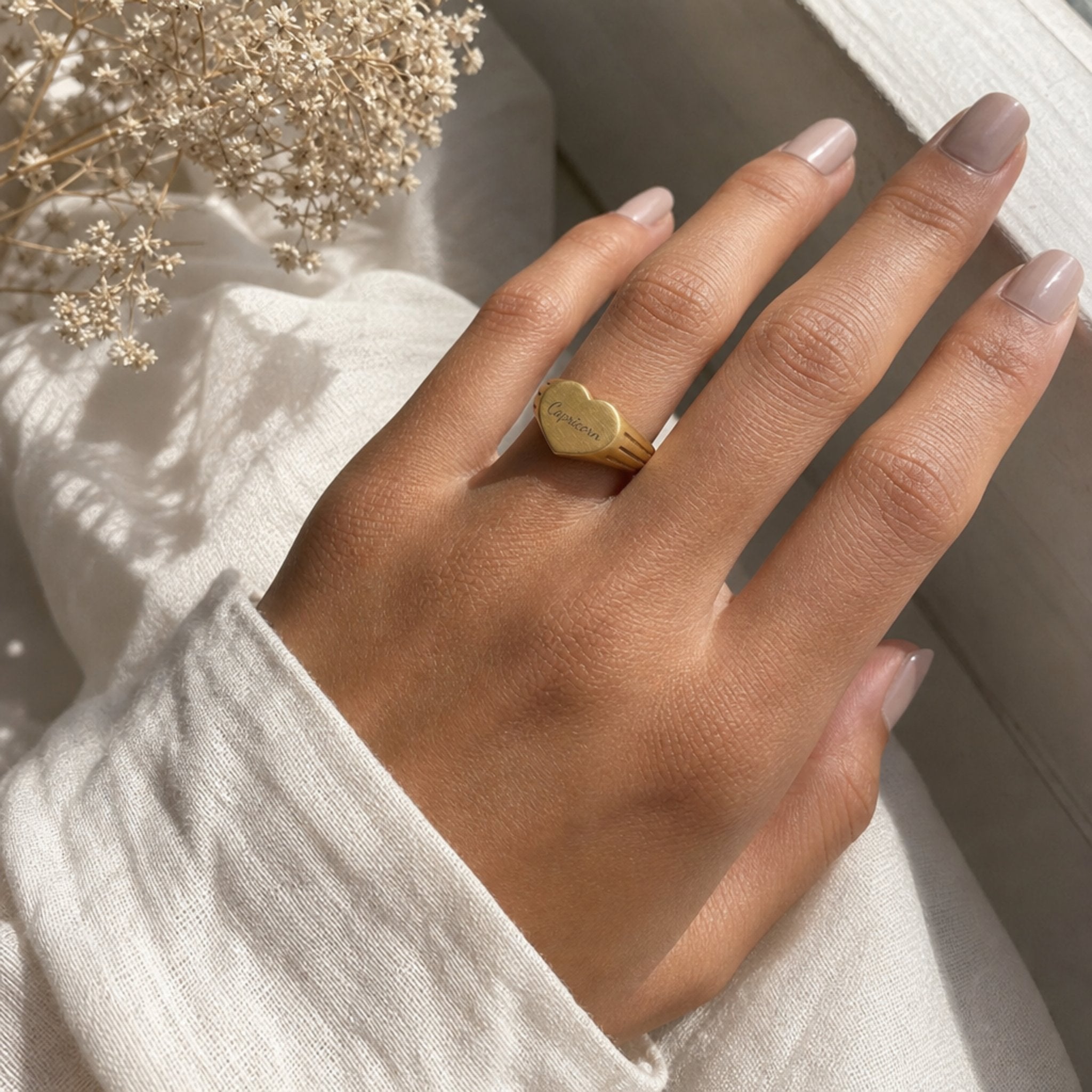 Capricorn zodiac heart signet ring on finger — model wearing engraved Capricorn heart signet, cream linen lifestyle moment