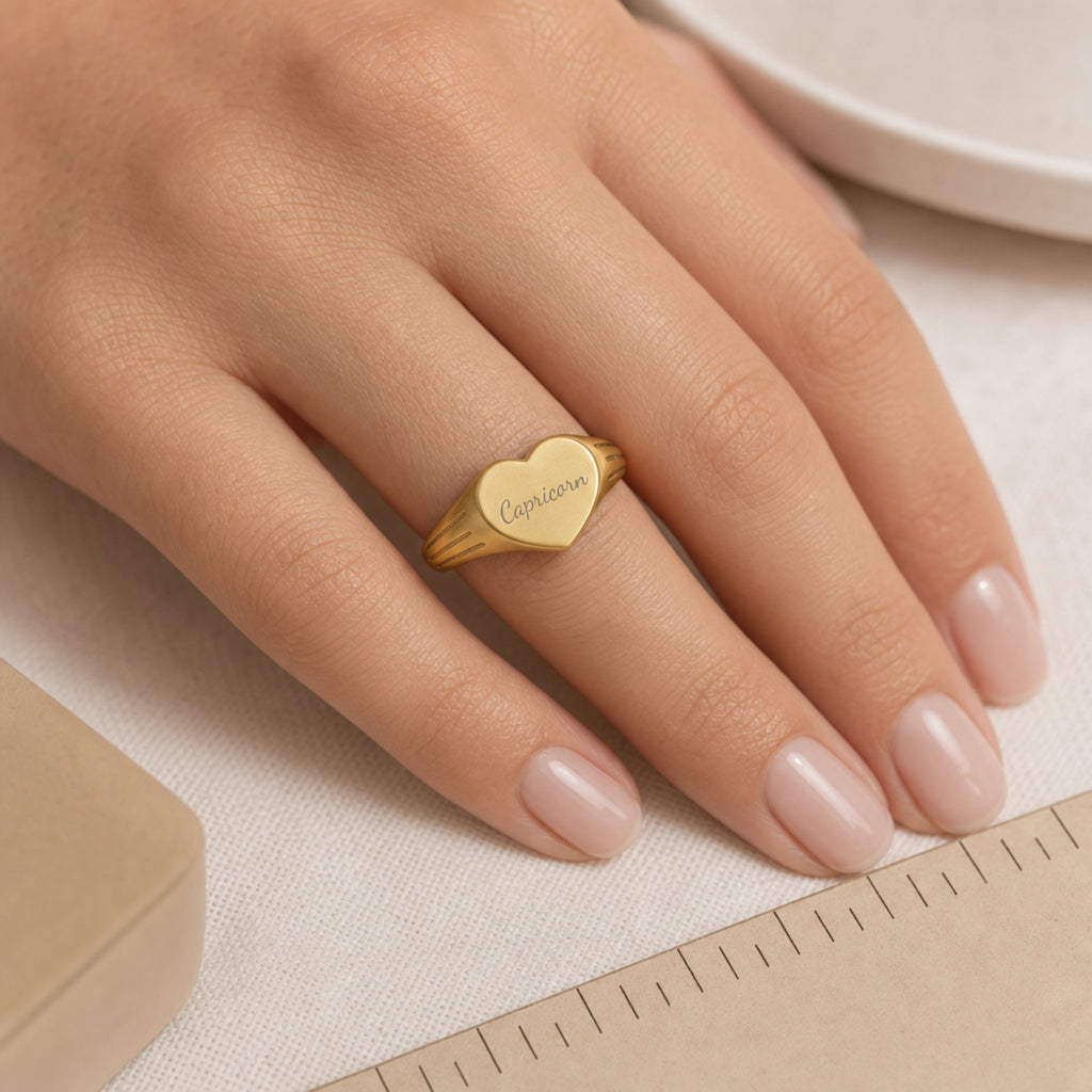 Capricorn zodiac heart signet ring scale-in-hand — fingers holding heart ring next to gift box and ruler, dainty signet sizing