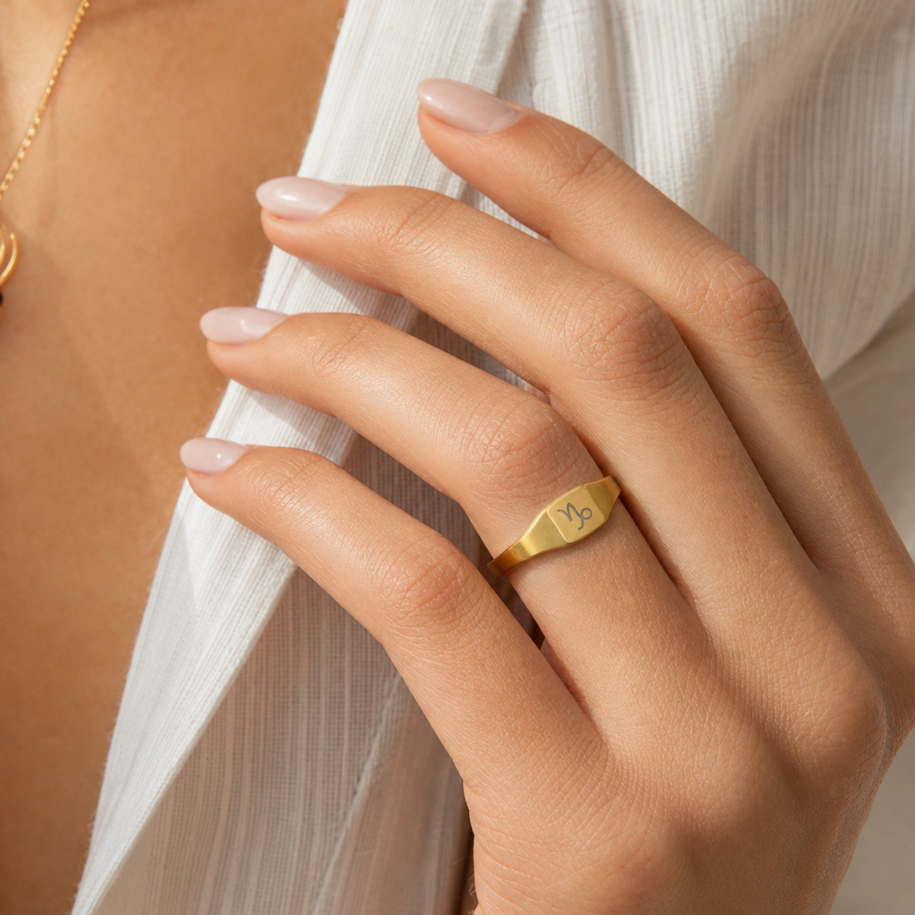 Capricorn zodiac square signet ring on finger — model wearing engraved Capricorn signet, cream linen lifestyle moment