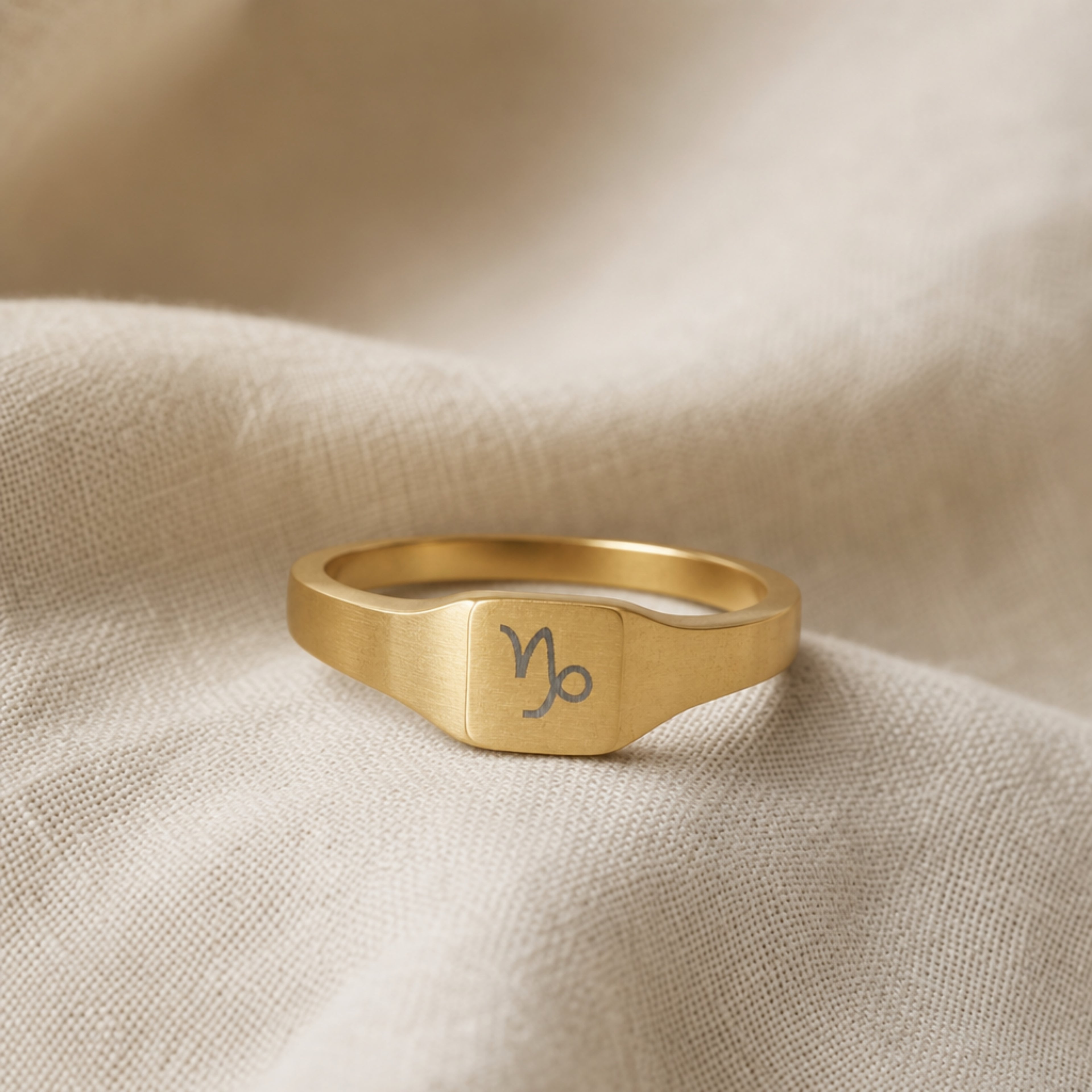 Capricorn zodiac square signet ring linen flatlay — engraved Goat ring on rumpled cream linen, editorial product shot