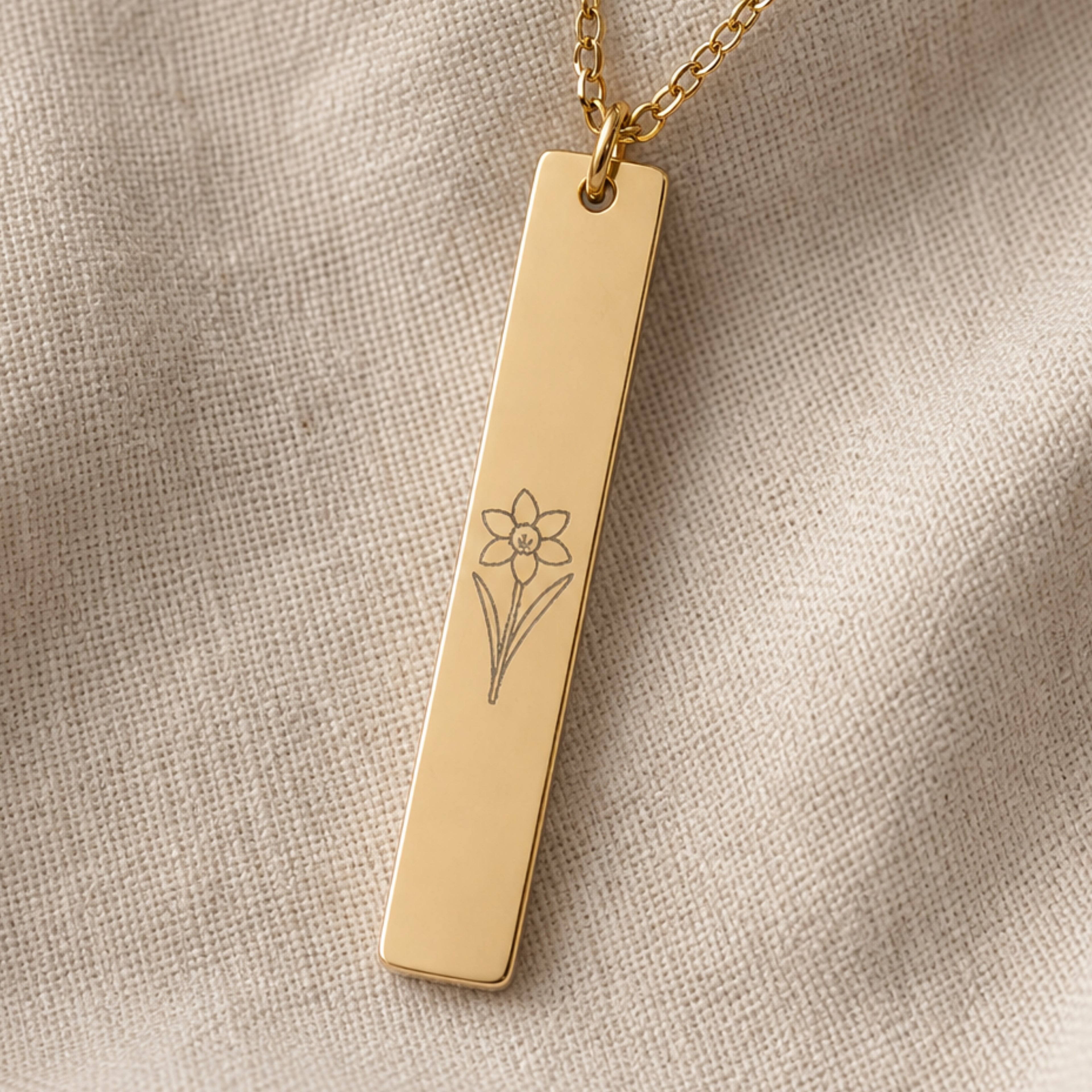 December birth flower necklace — Narcissus engraved vertical bar pendant flatlay with dried botanicals on cream linen