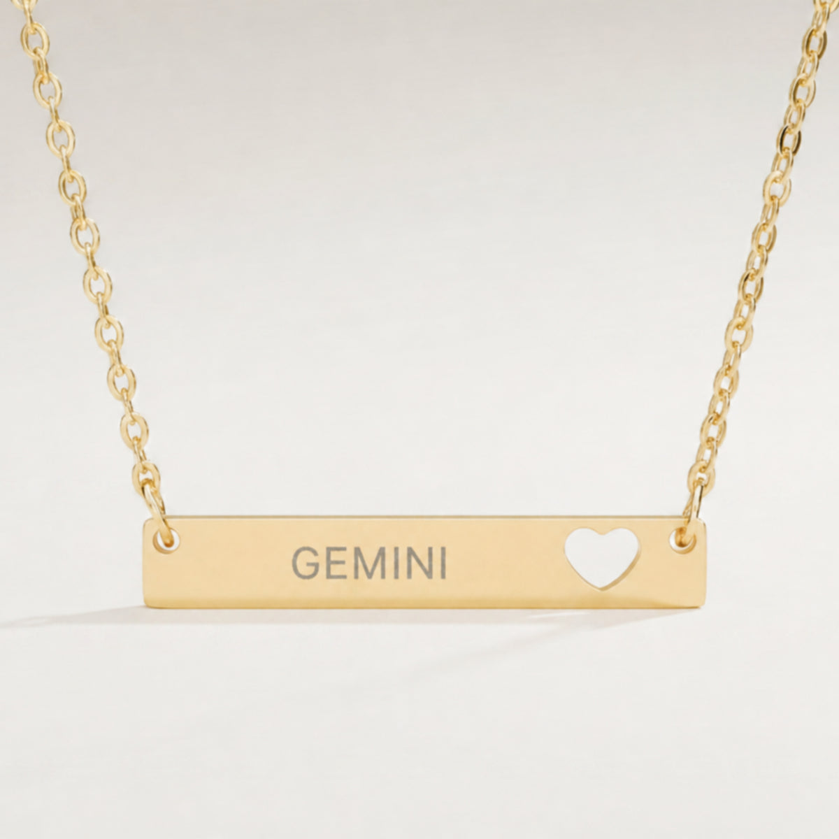 Gemini zodiac necklace — engraved cutout heart bar pendant, premium close-up macro hero, 18K Gold PVD, grey laser-etched GEMINI
