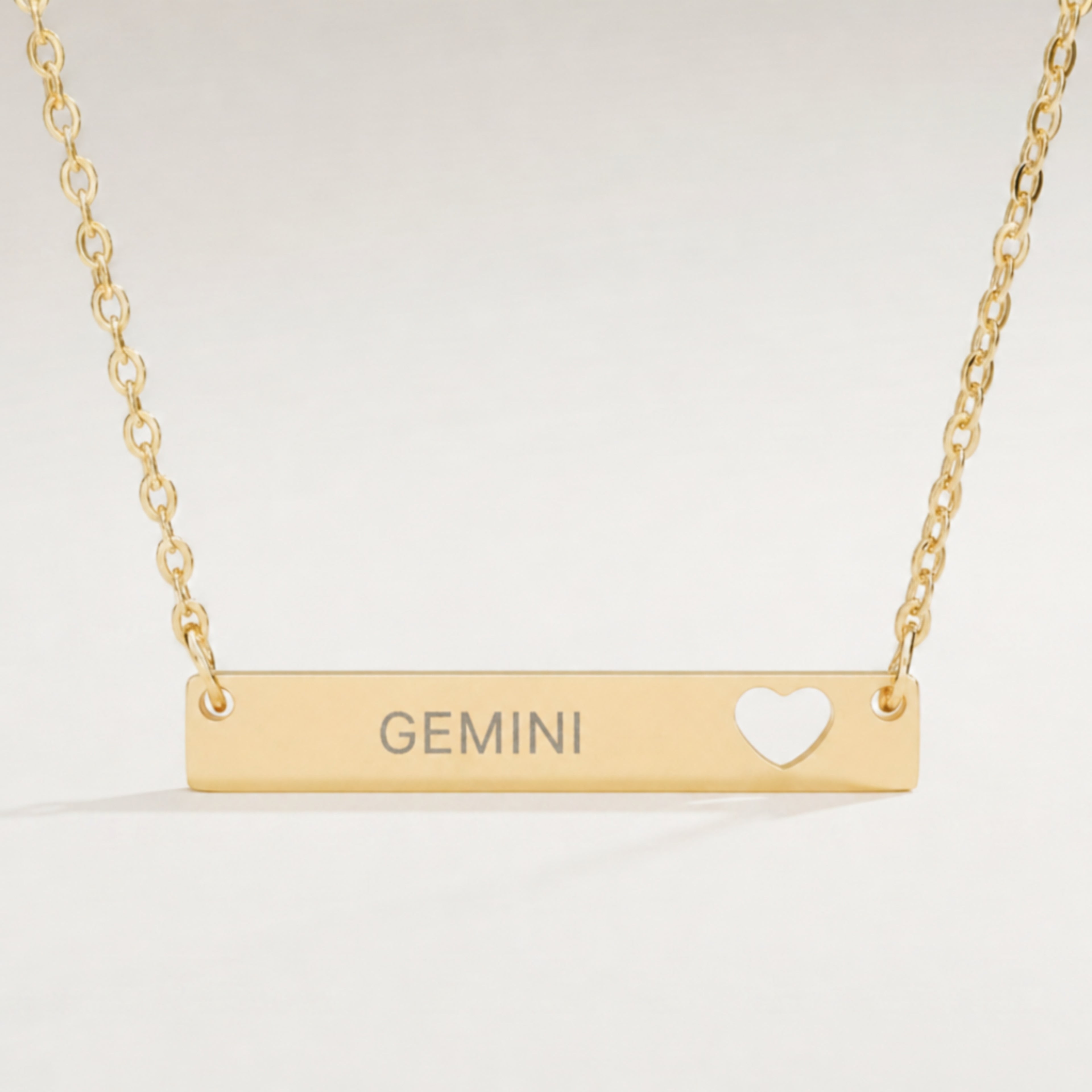 Gemini zodiac necklace — engraved cutout heart bar pendant, premium close-up macro hero, 18K Gold PVD, grey laser-etched GEMINI