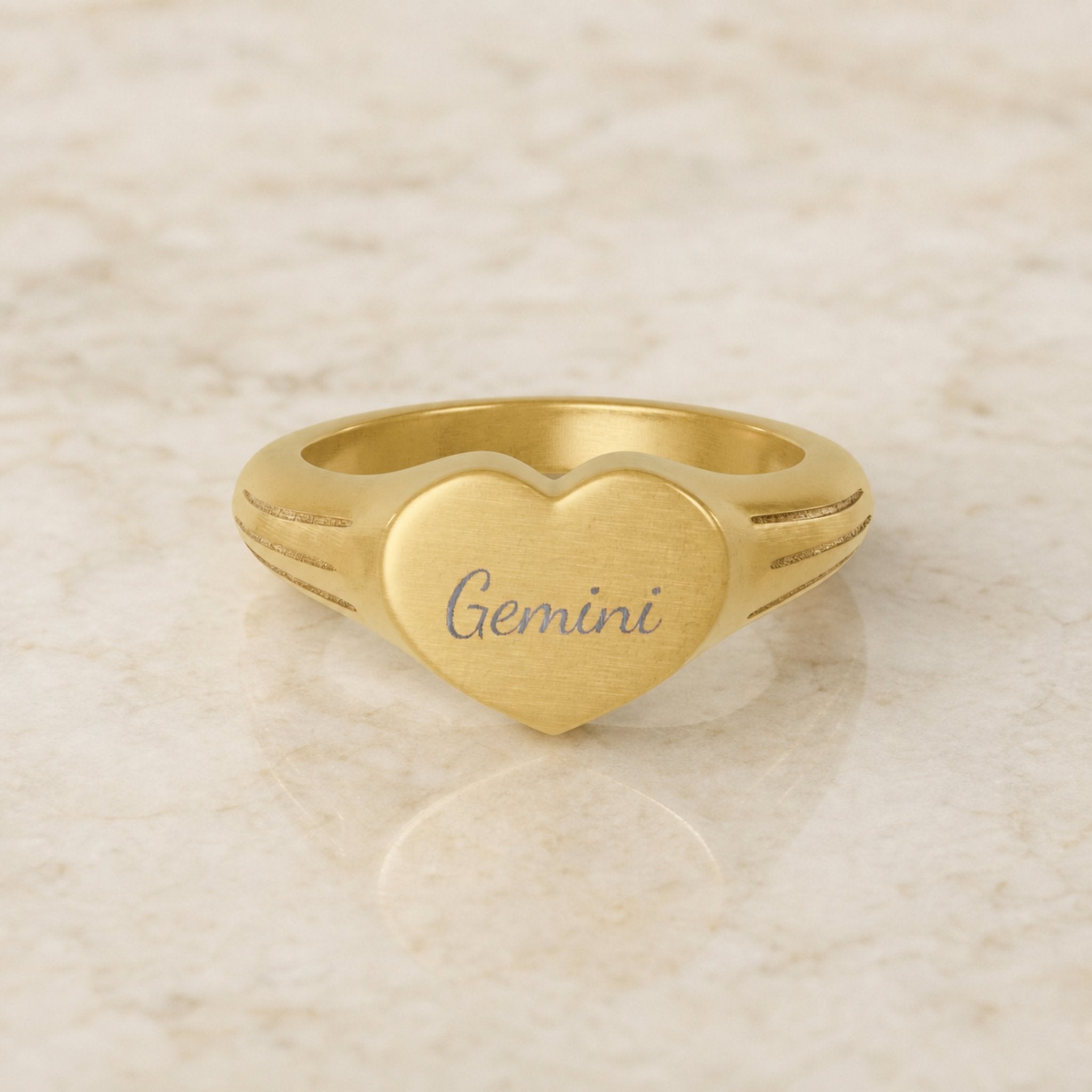 Gemini zodiac heart signet ring — hero macro of laser-engraved Gemini name in Dancing Script cursive on 18K gold heart face