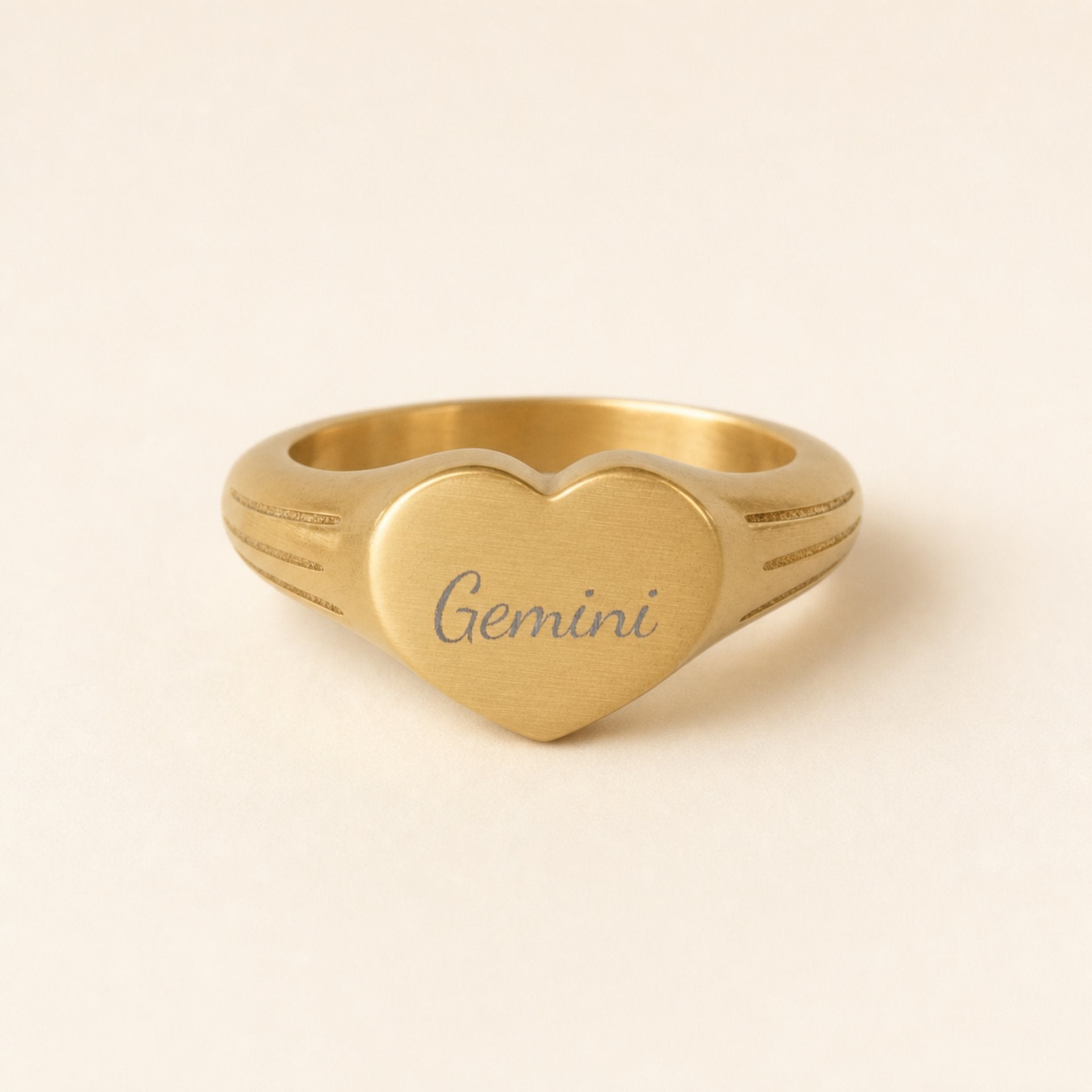 Gemini zodiac heart signet ring studio front — clean cream backdrop product shot, 18K gold matte PVD