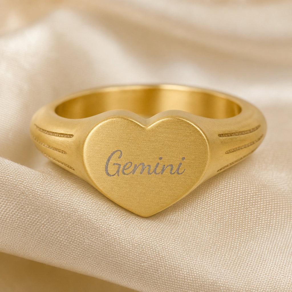 Gemini zodiac heart signet ring engraving close-up — laser-etched Gemini name detail, brushed grey cursive on matte gold heart