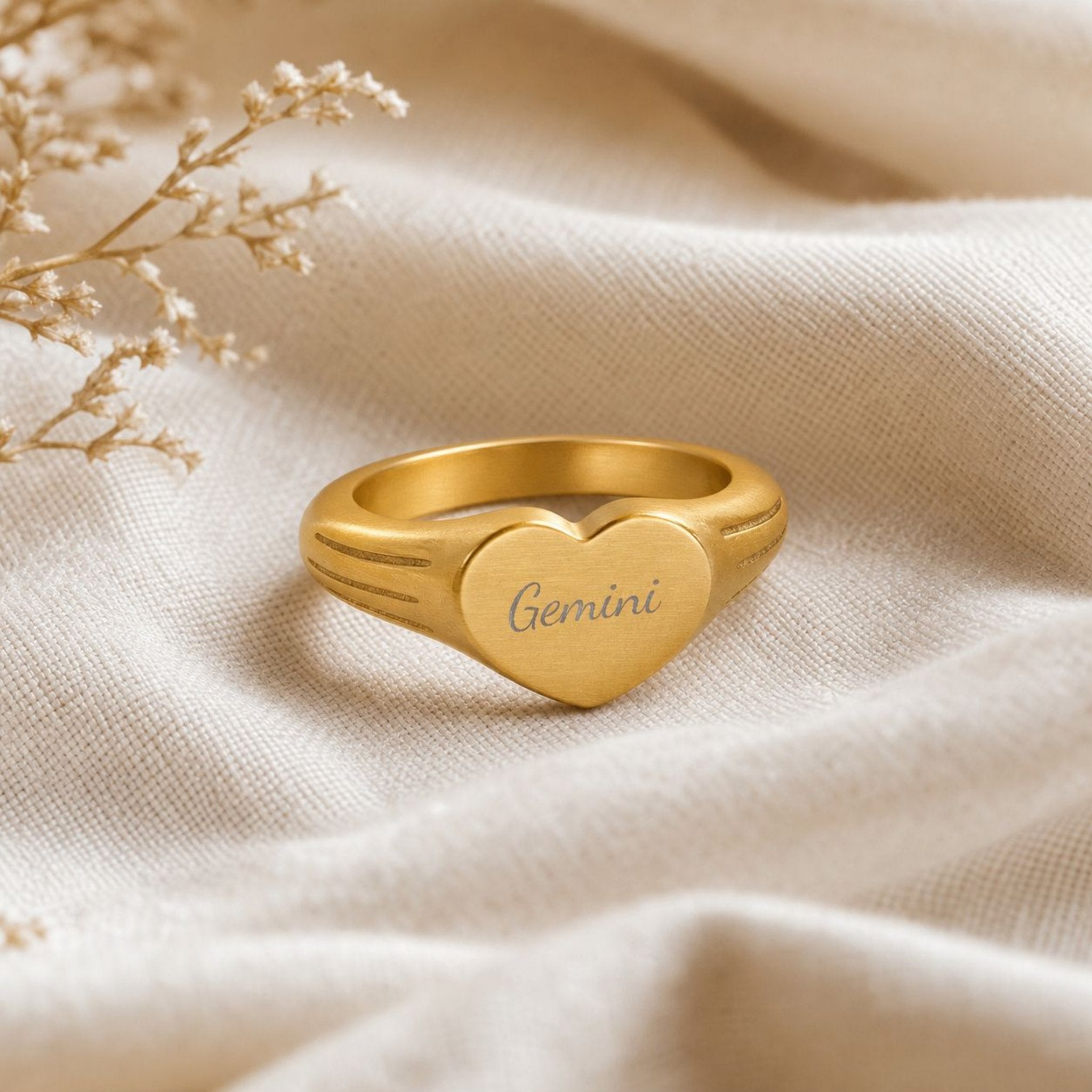 Gemini zodiac heart signet ring linen flatlay — engraved Gemini heart ring on rumpled cream linen with dried floral, editorial styling