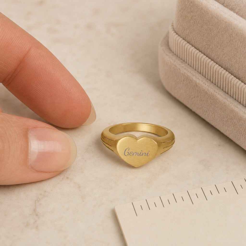 Gemini zodiac heart signet ring scale-in-hand — fingers holding heart ring next to gift box and ruler, dainty signet sizing