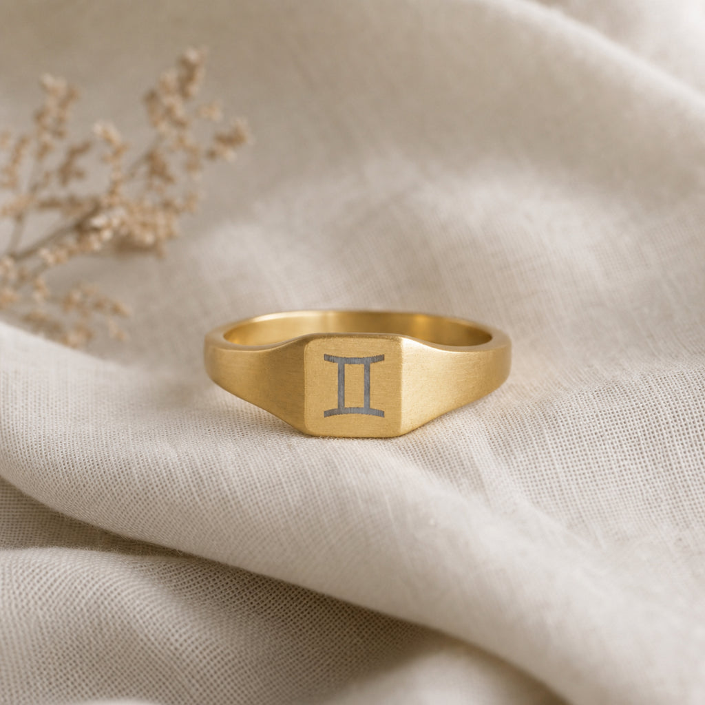 Gemini zodiac square signet ring linen flatlay — engraved Twins ring on rumpled cream linen, editorial product shot