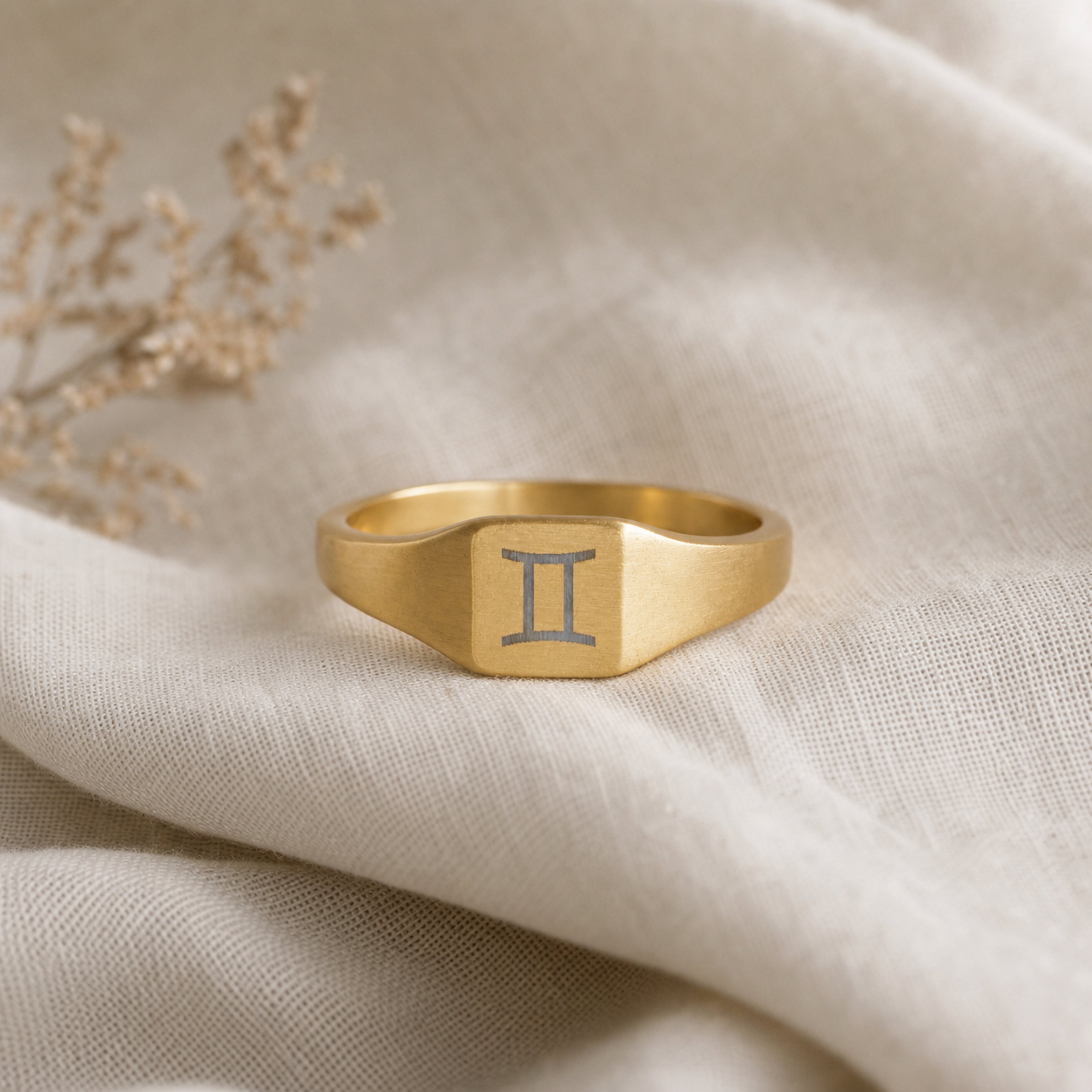 Gemini zodiac square signet ring linen flatlay — engraved Twins ring on rumpled cream linen, editorial product shot