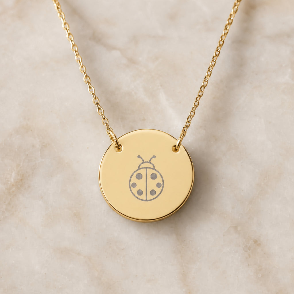 Dainty engraved ladybug coin necklace in 18K gold PVD — laser-engraved ladybug on round pendant, warm cream lifestyle