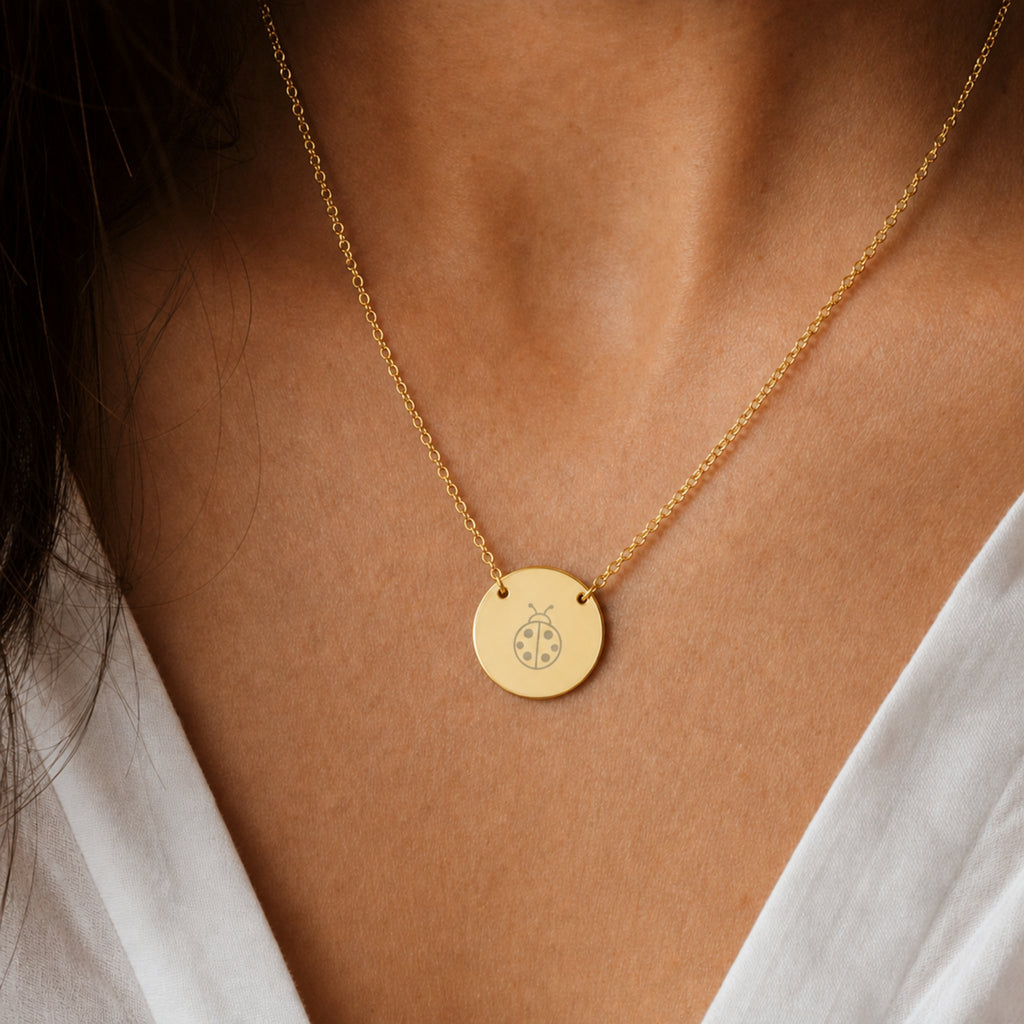 Dainty engraved ladybug coin necklace in 18K gold PVD — laser-engraved ladybug on round pendant, warm cream lifestyle