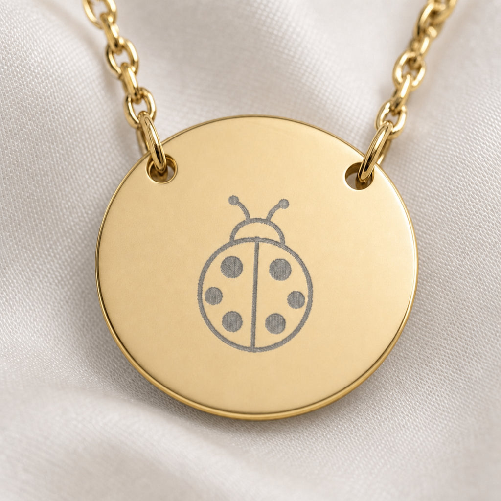 Dainty engraved ladybug coin necklace in 18K gold PVD — laser-engraved ladybug on round pendant, warm cream lifestyle