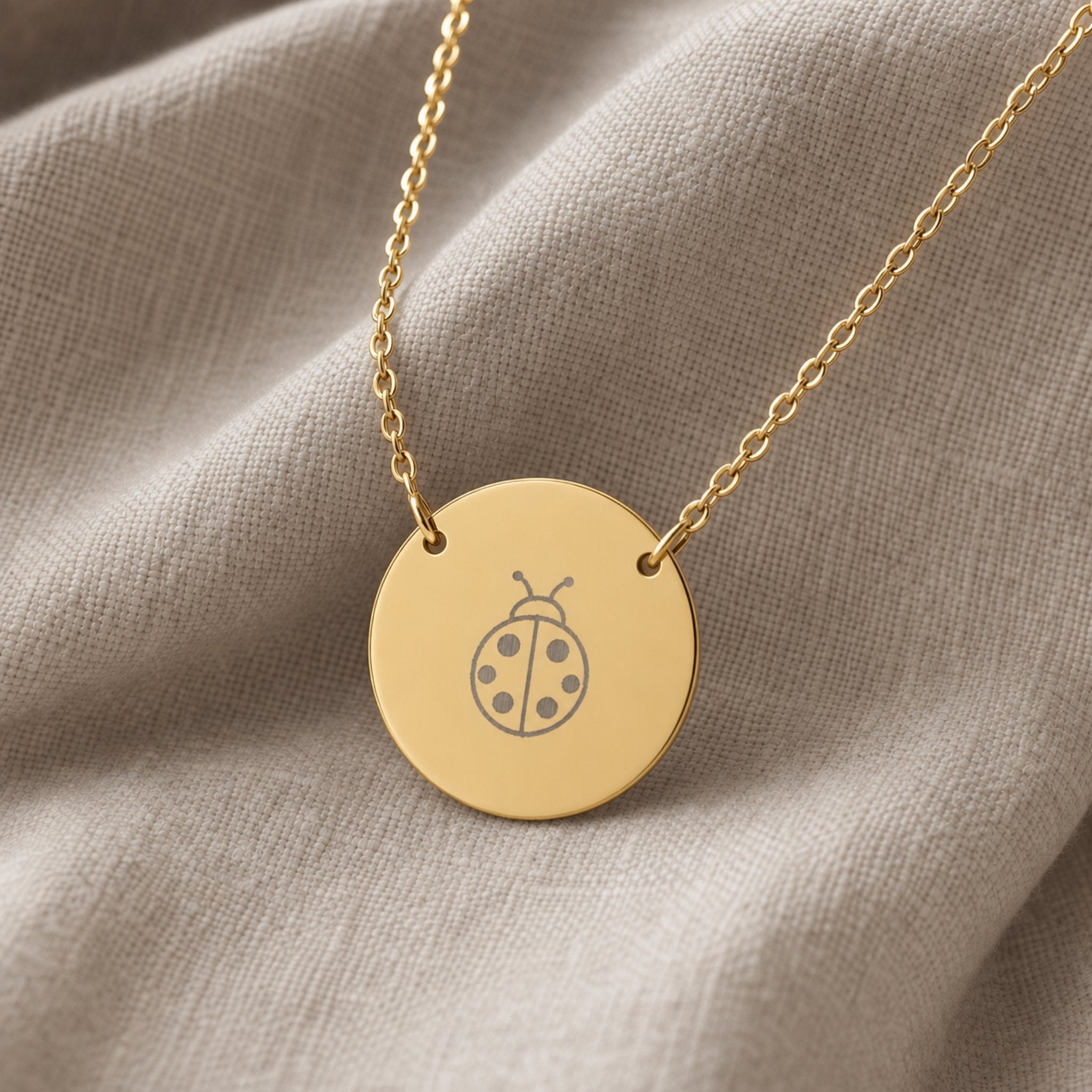 Dainty engraved ladybug coin necklace in 18K gold PVD — laser-engraved ladybug on round pendant, warm cream lifestyle
