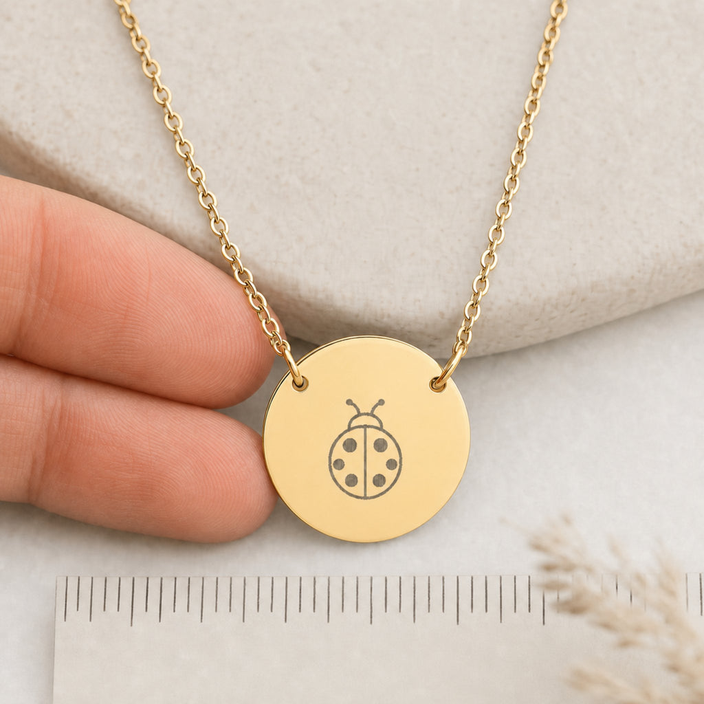 Dainty engraved ladybug coin necklace in 18K gold PVD — laser-engraved ladybug on round pendant, warm cream lifestyle