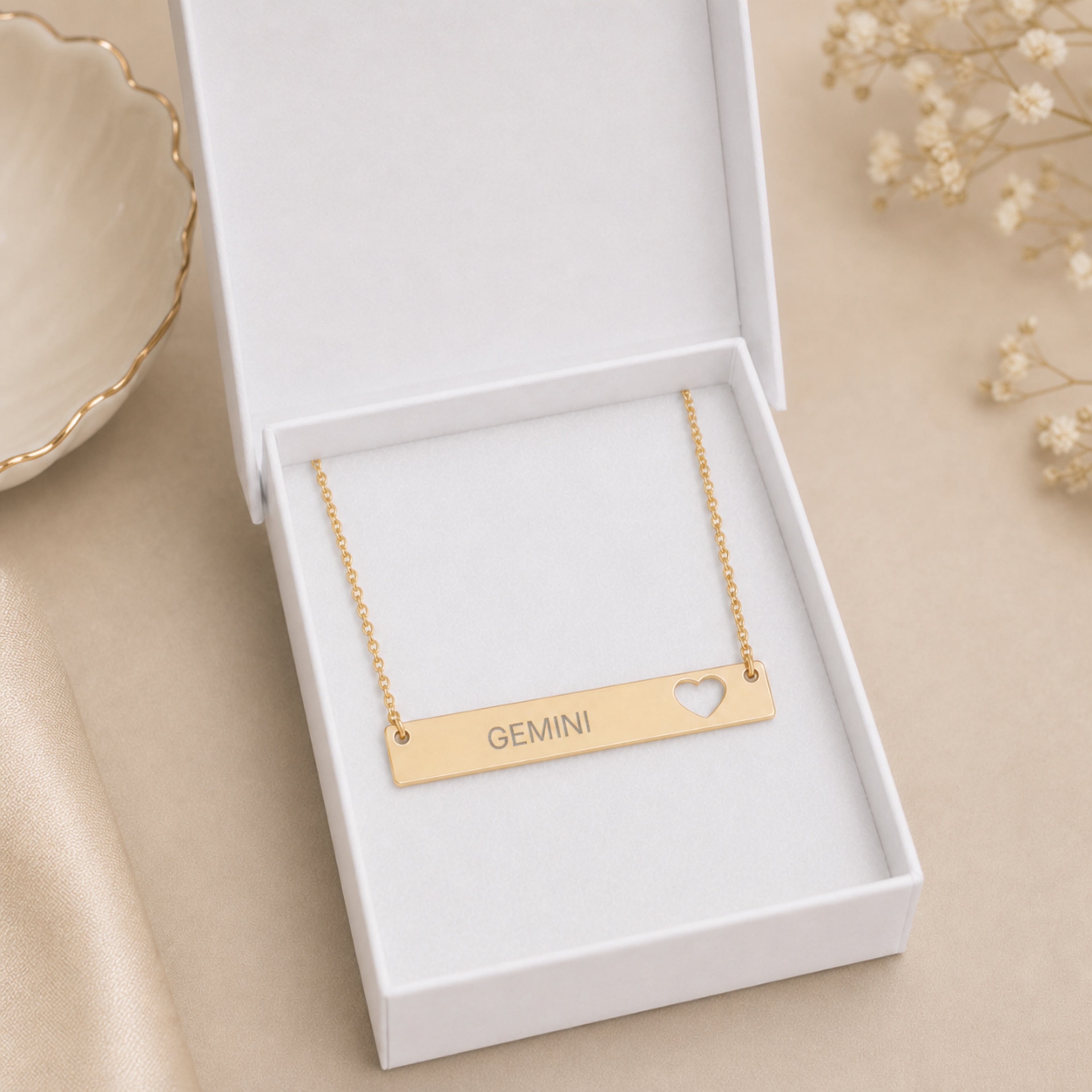 The Gemini zodiac necklace nestled in Memory That Lasts signature cream gift box — 18K Gold cutout heart bar pendant with grey laser-etched GEMINI, premium unboxing moment (AI-generated image)