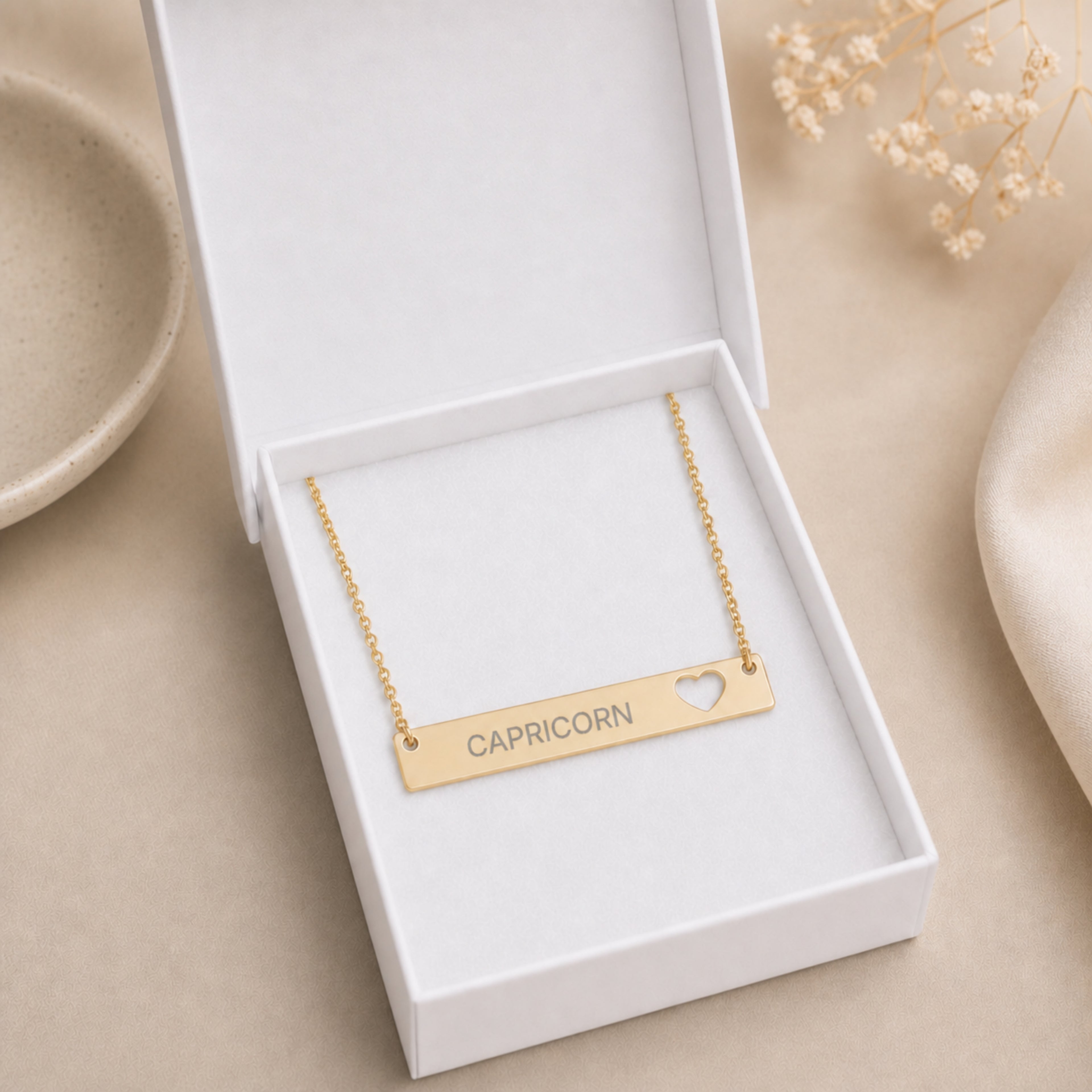 The Capricorn zodiac necklace nestled in Memory That Lasts signature cream gift box — 18K Gold cutout heart bar pendant with grey laser-etched CAPRICORN, premium unboxing moment (AI-generated image)