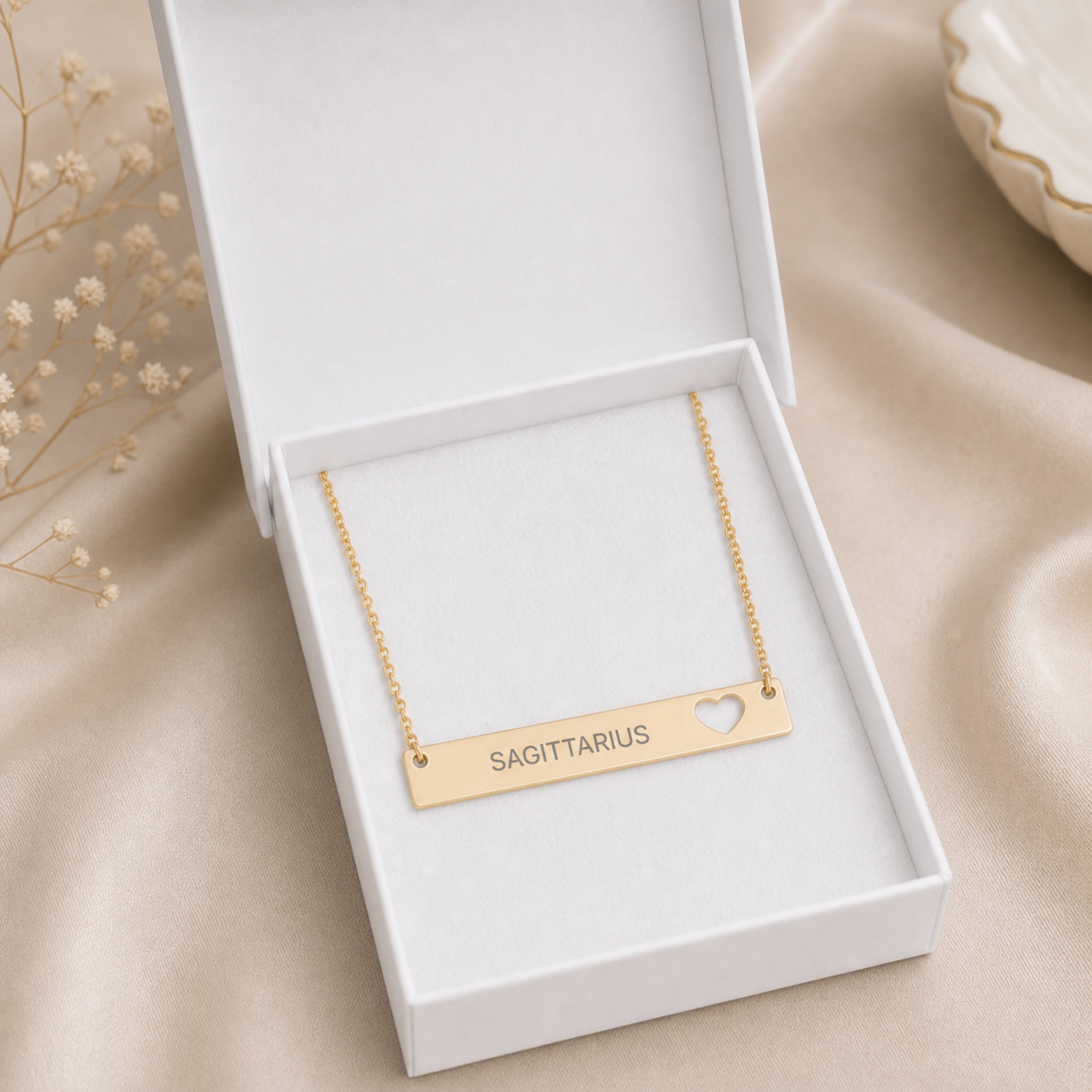 The Sagittarius zodiac necklace nestled in Memory That Lasts signature cream gift box — 18K Gold cutout heart bar pendant with grey laser-etched SAGITTARIUS, premium unboxing moment (AI-generated image)