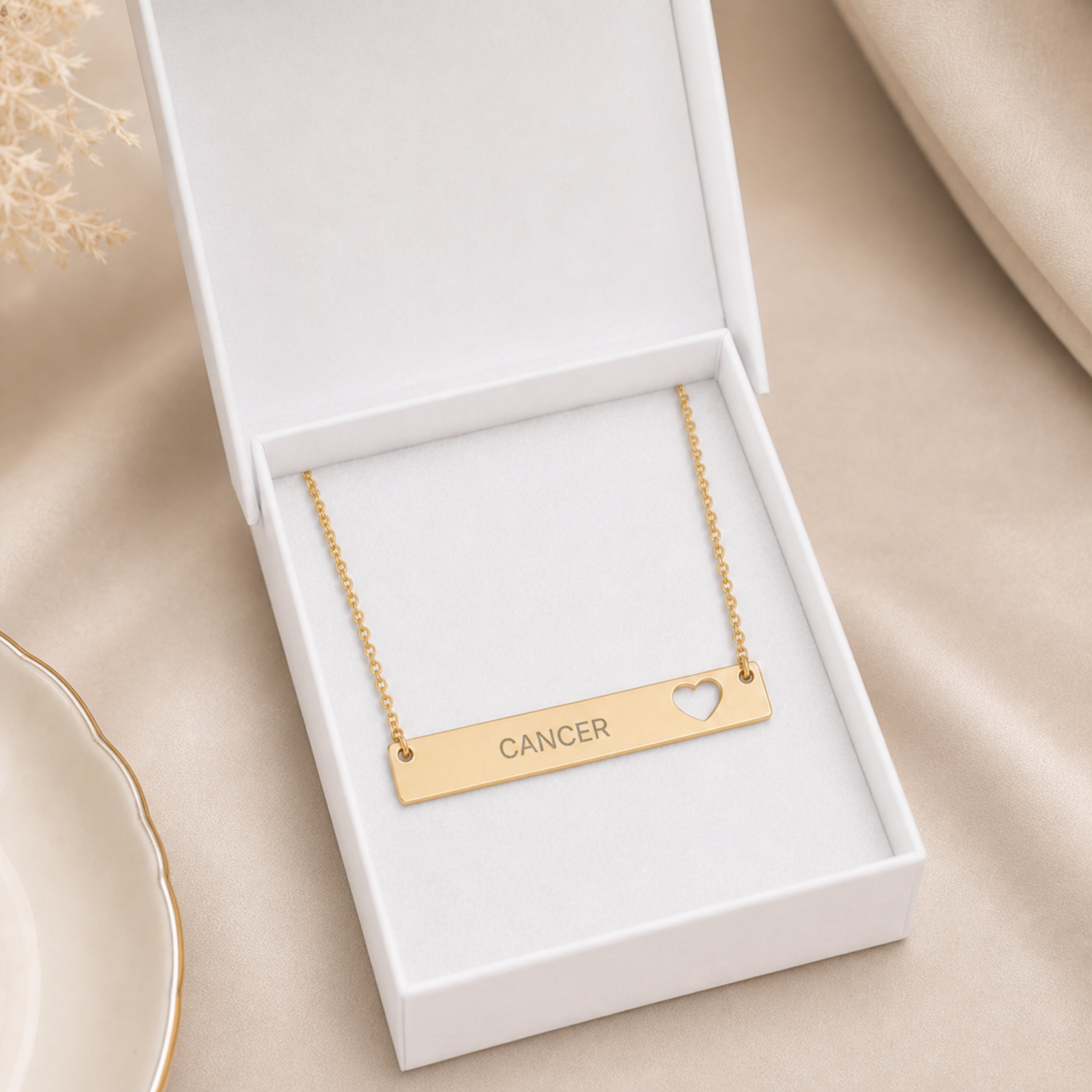The Cancer zodiac necklace nestled in Memory That Lasts signature cream gift box — 18K Gold cutout heart bar pendant with grey laser-etched CANCER, premium unboxing moment (AI-generated image)