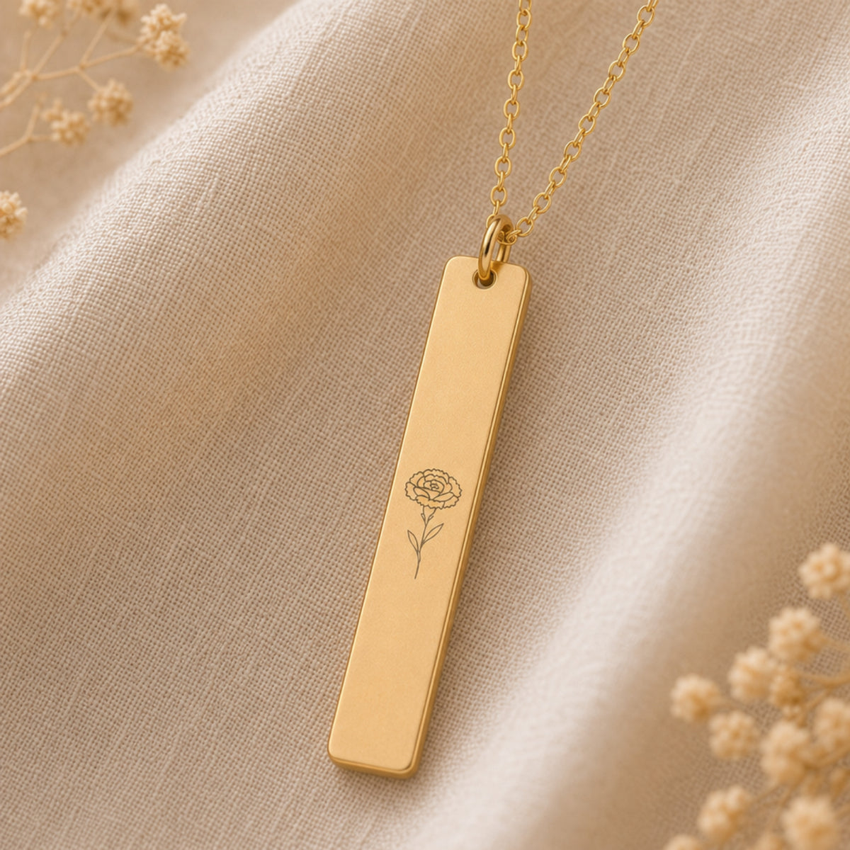 January birth flower necklace — Carnation engraved vertical bar pendant flatlay with dried botanicals on cream linen, premium editorial styling, 18K Gold PVD on premium 316L stainless steel
